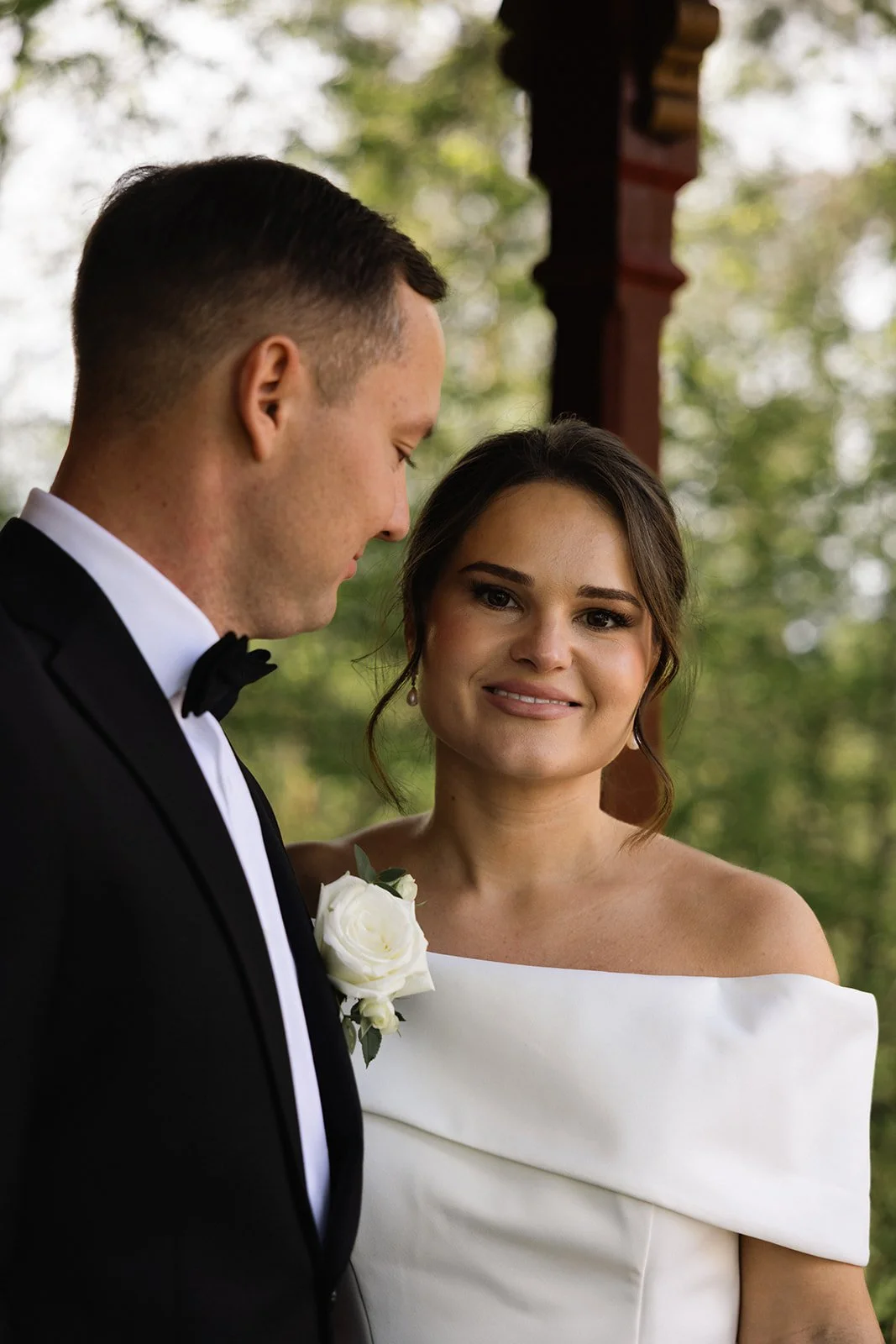 Et brudepar ved bryllupsceremoni, der står under en trekantet trehytte med grønne trær i bakgrunnen