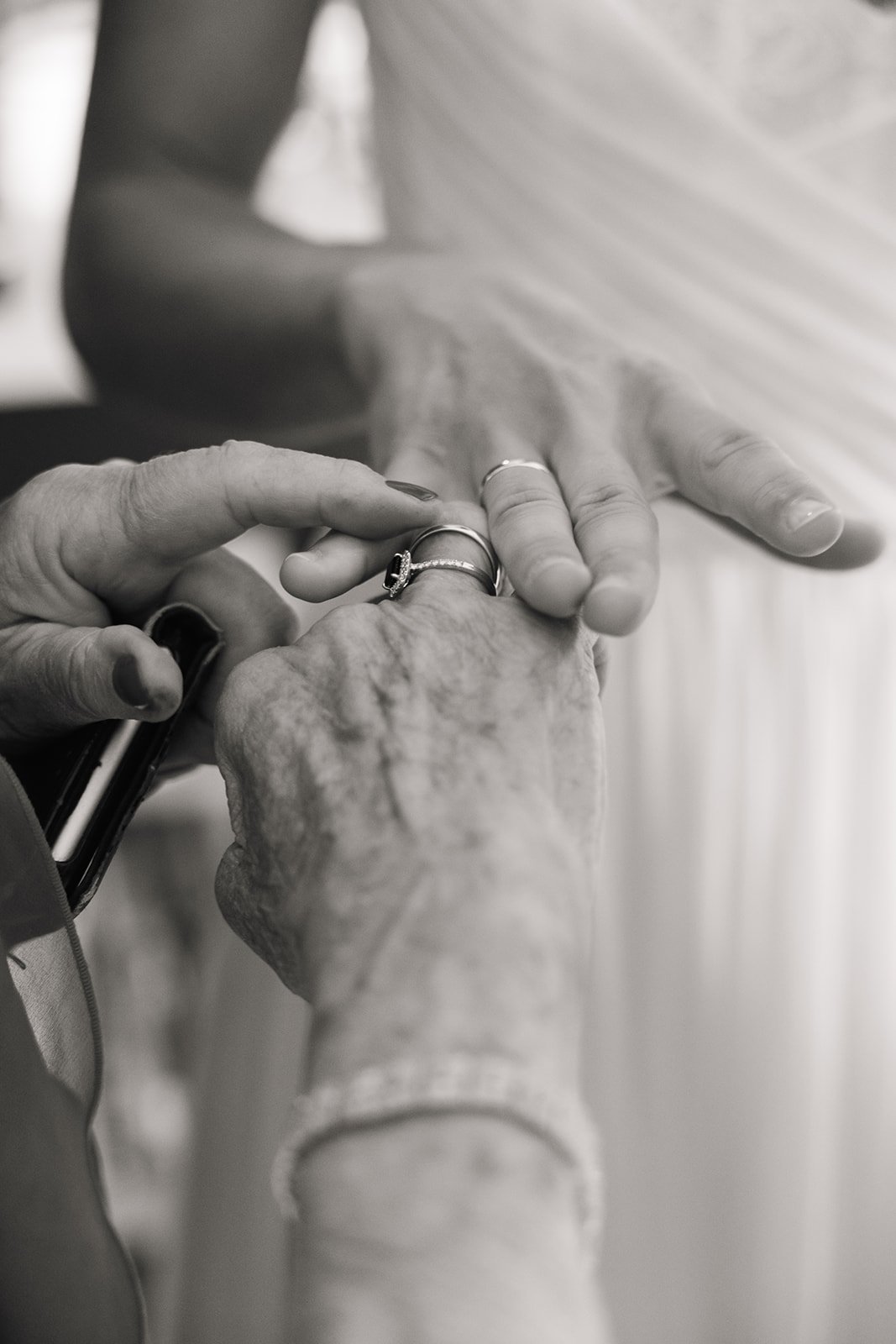 To eldre hender holder hverandre, én hånd med ringer støttes av en yngre hånd. Det er et svart-hvitt bilde.