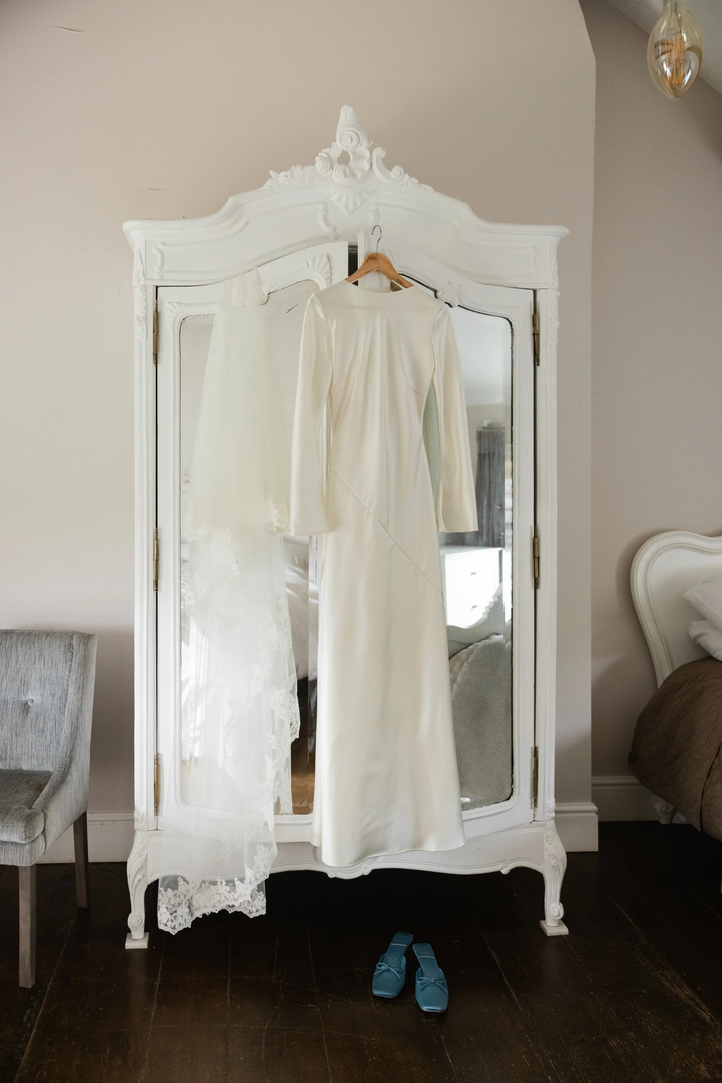 En hvit brudekjole og et brudekjole underkjole eller slør henger på en hvit speilskap. Det er også et par blå sko plassert på gulvet foran speilskapet.