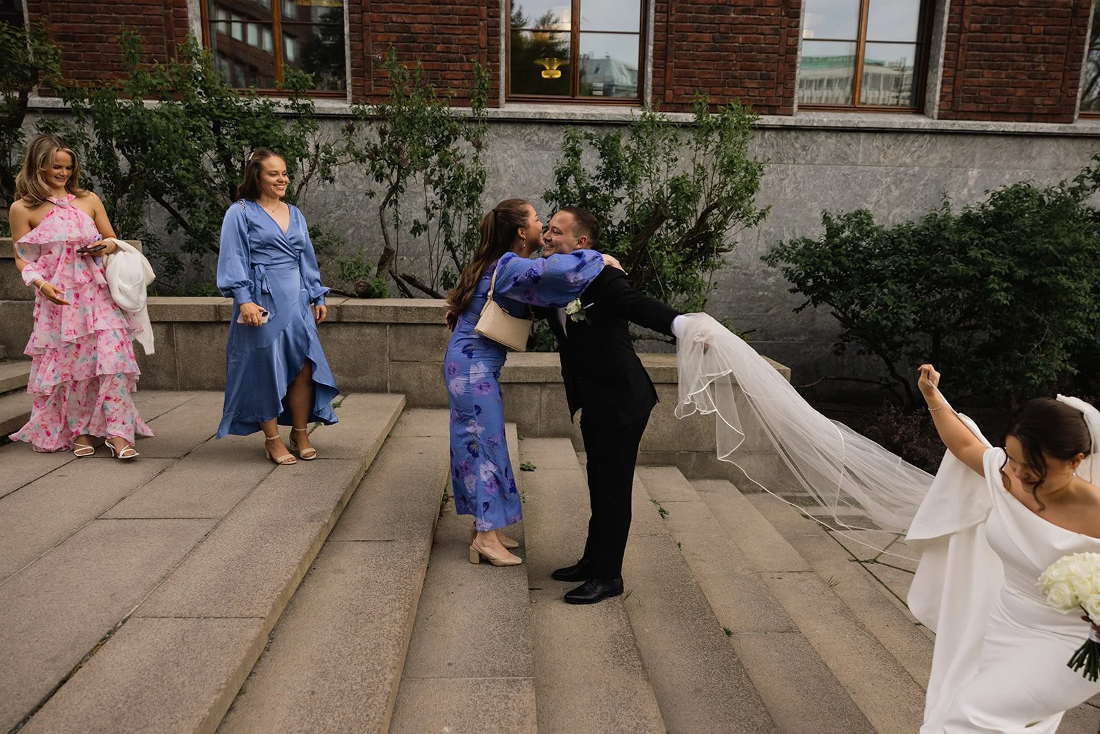 En bryllupsfeiring med et par som kysser på trappen, omgitt av venner og familie.