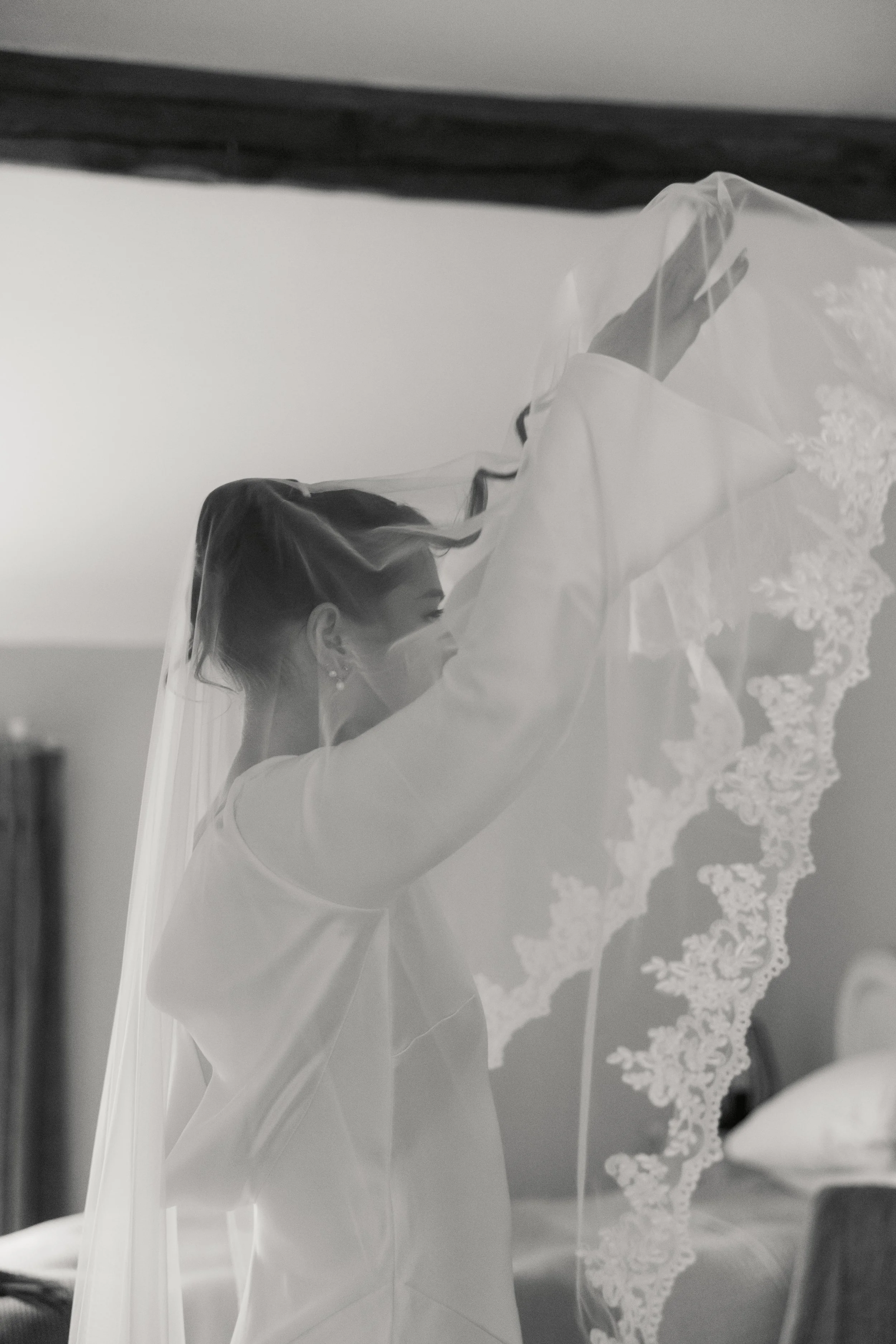 En kvinne med brunt hår og ørepynt som holder opp en brudekappe med blondedetaljer.