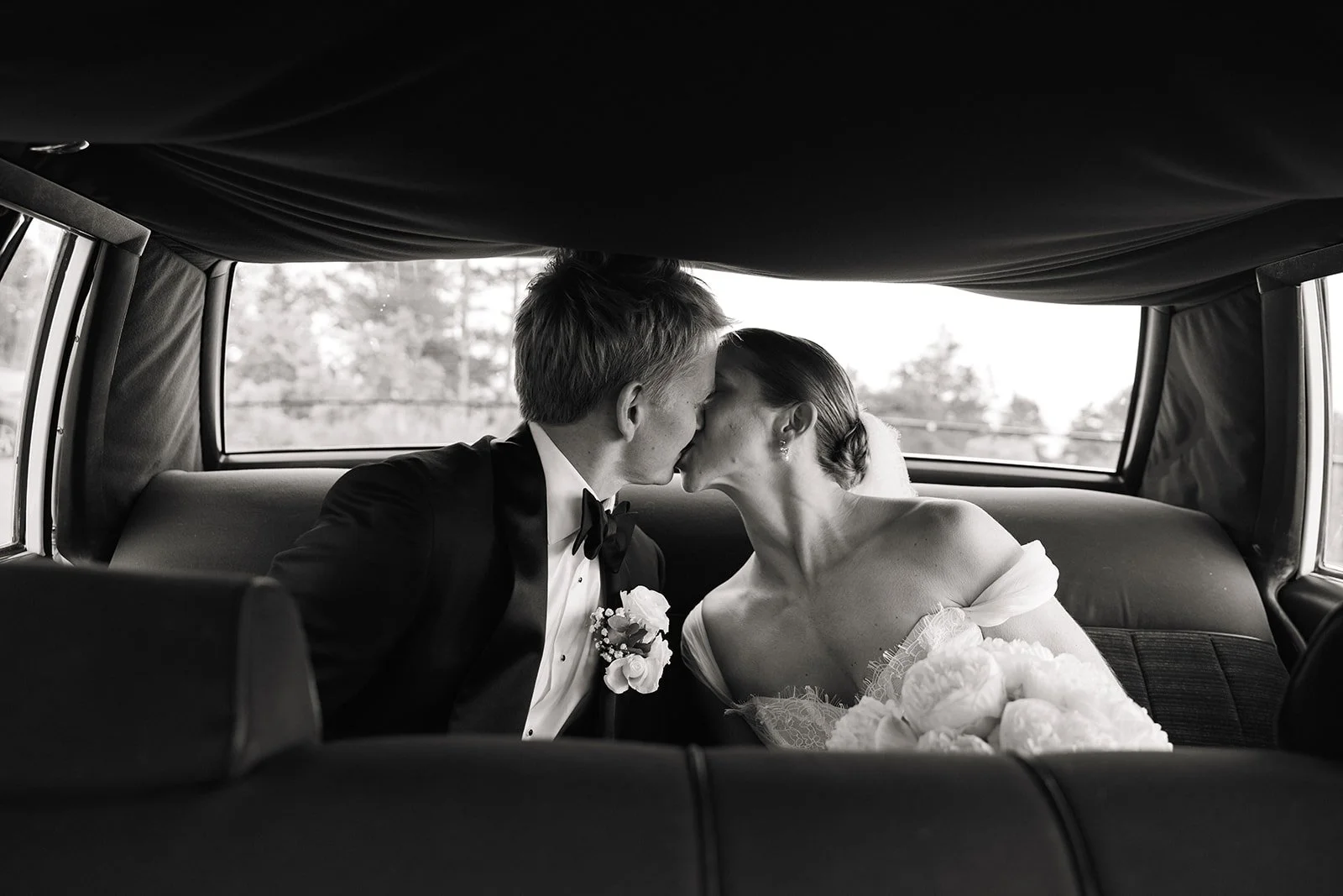 Et brudepar kysser i baksetet av en bil, i svart-hvitt.