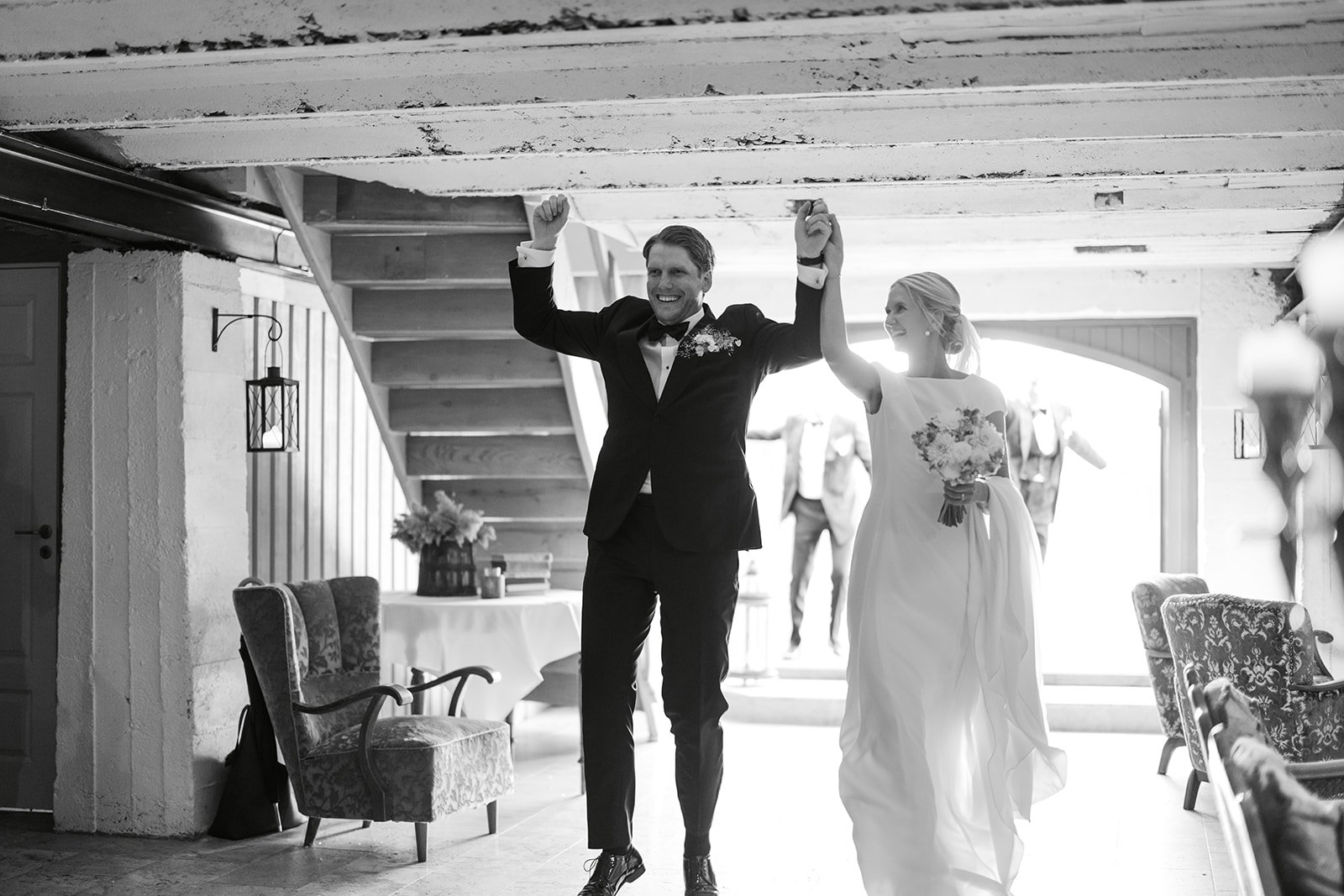 Den nygifte bruden og brudgommen rir inn i rommet, smilende med armene løftet i glede.