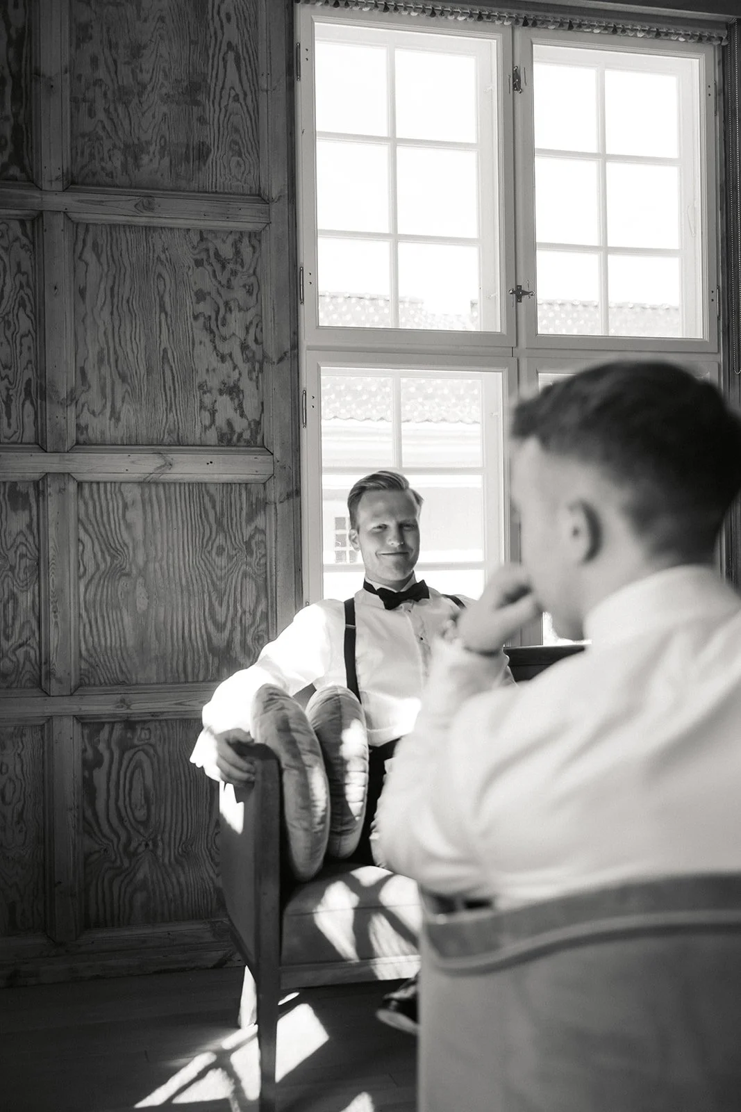 To menn i hvite skjorter og svarte bånd i et rom med trekledte vegger og store vinduer.