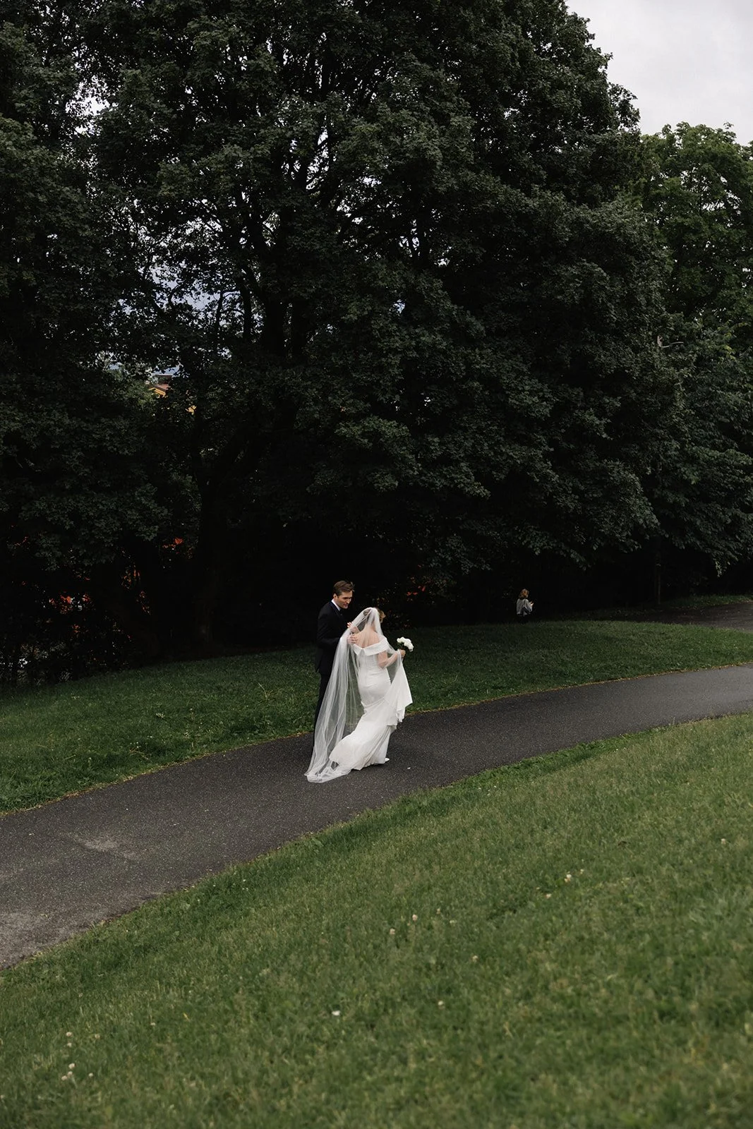 Et GIF av et bryllupsmaleri med en brud og brudgom som går på en sti i en park med store trær i bakgrunnen.