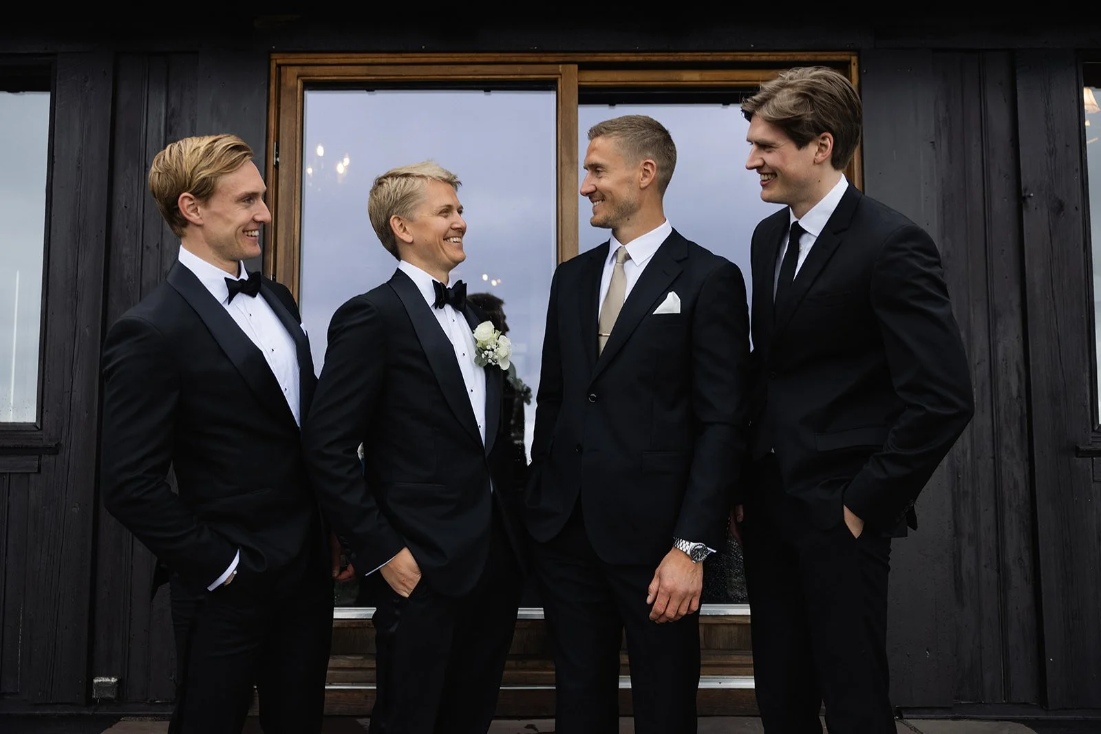 Fem menn i formelle klær står og snakker foran en svart bygningsvegg med et vindu bak.