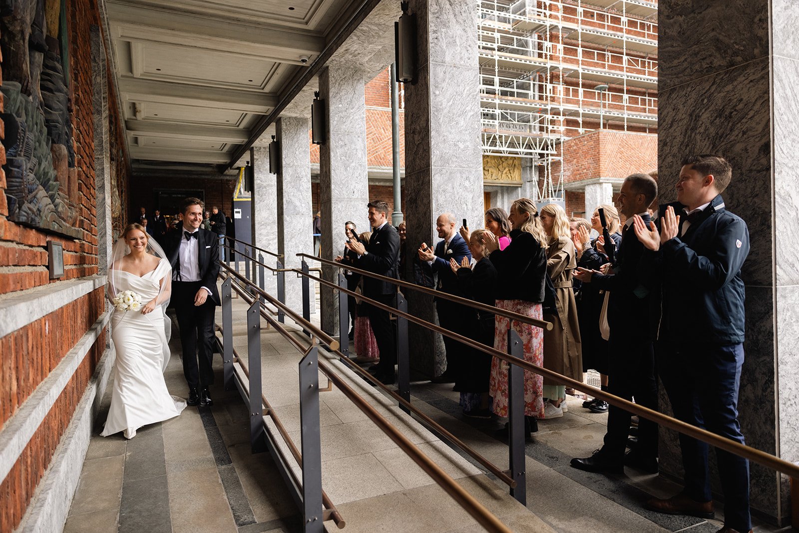 Bryllupspar går inn under en dekkende tak, mens gjestene står og tar bilder og applauderer.