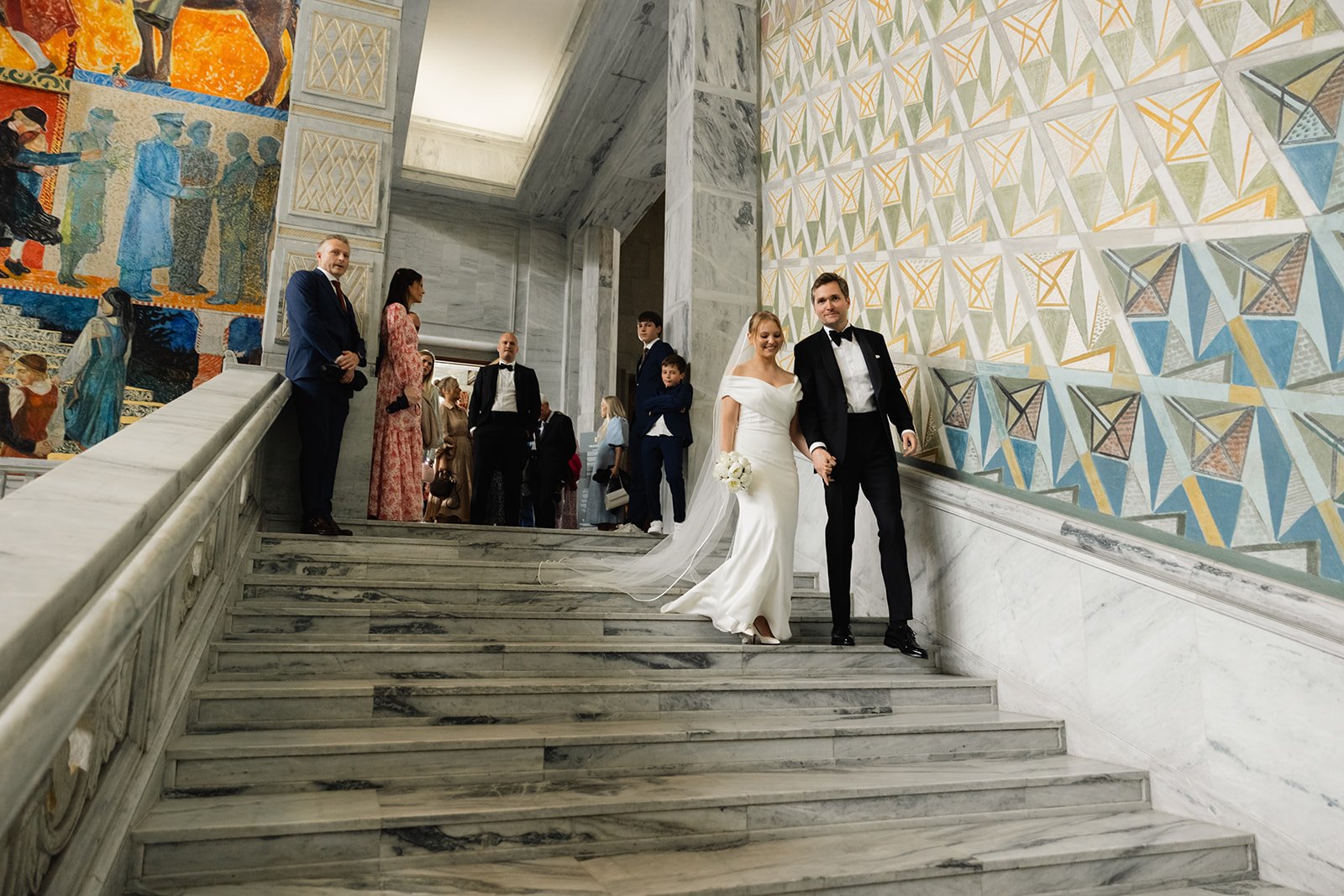 Nylig gifte par som går ned en marmor-trapp i en historisk bygning, omgitt av gjester.