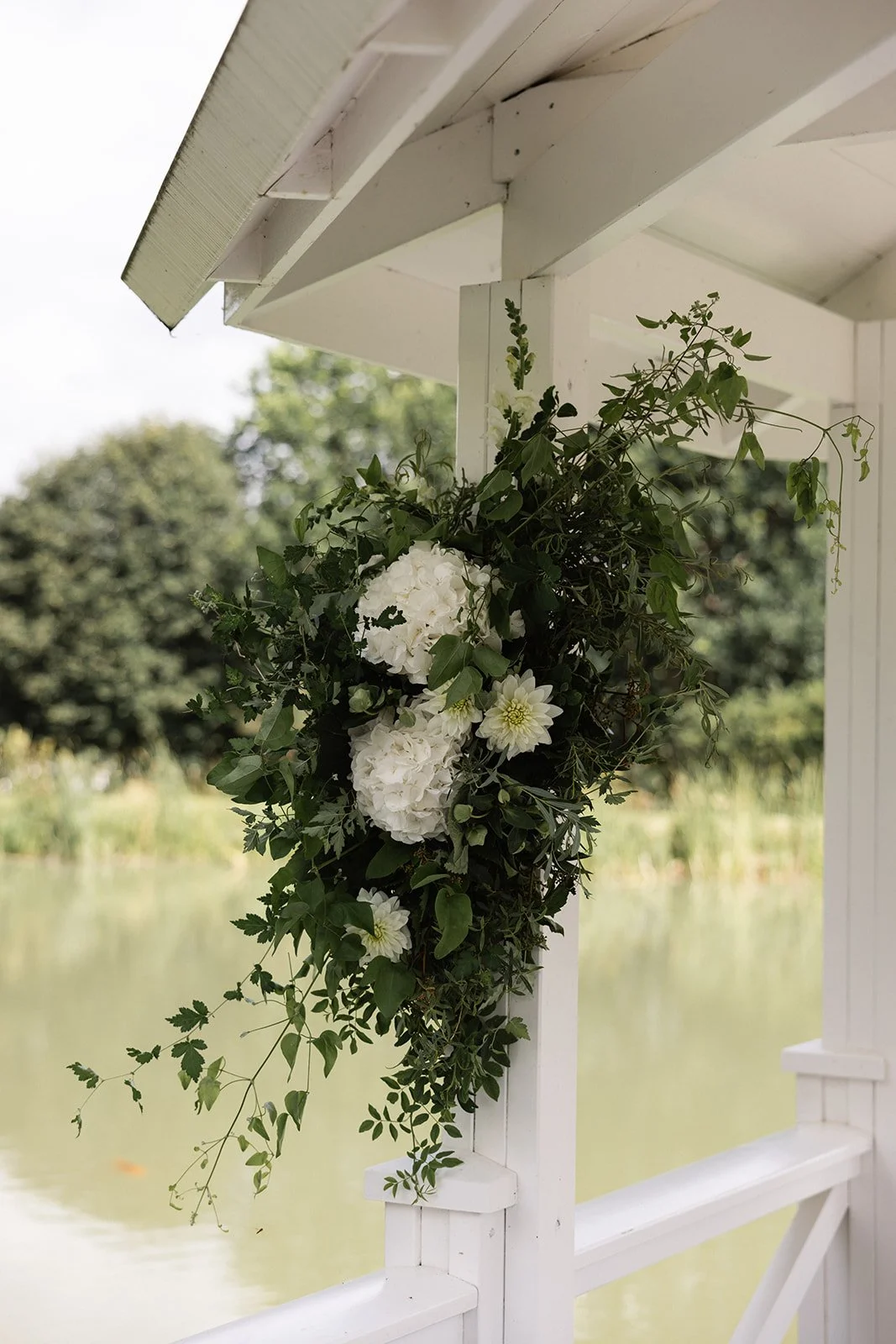 hvordan en blomsterdekorasjon av hvite blomster og grønne blader er festet til et hvitt lyst gjerde på utendørs uteplass