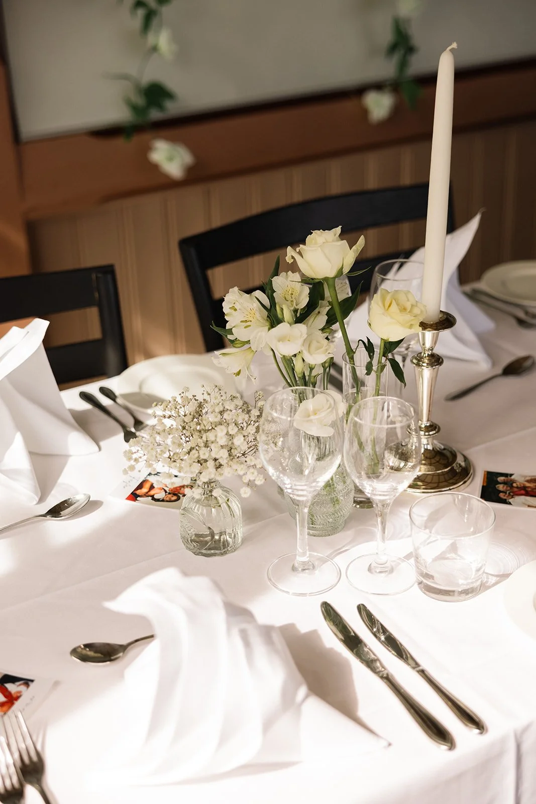 Elegant borddekorasjon med hvite blomster, lys med kandekorstake, glass, bestikk og tepper for en formell begivenhet.