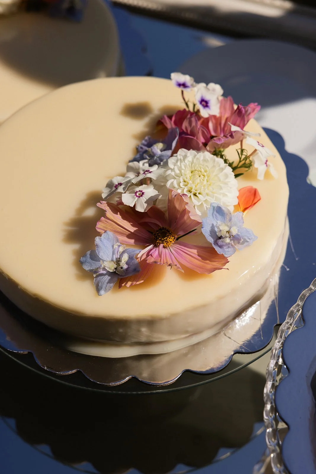 En rund hvit kake med blomsterdekorasjon på toppen, plassert på en sølvfarget kakefat.