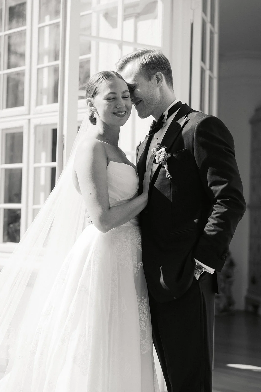 Et lykkelig brudepar som står tett sammen innendørs, med vinduer i bakgrunnen, under bryllupscermoni.
