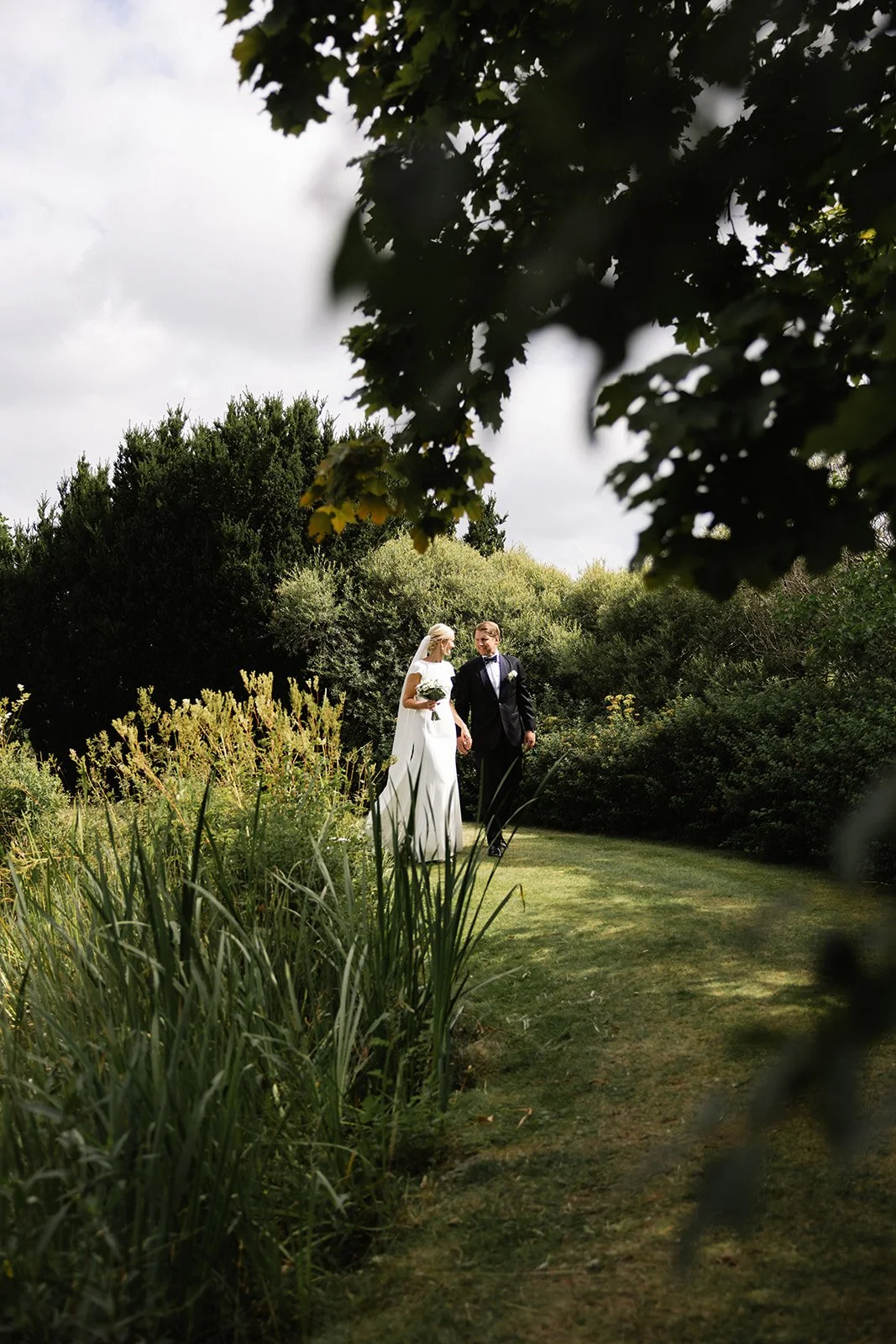 Et brudepar går hånd i hånd på en grønn hage