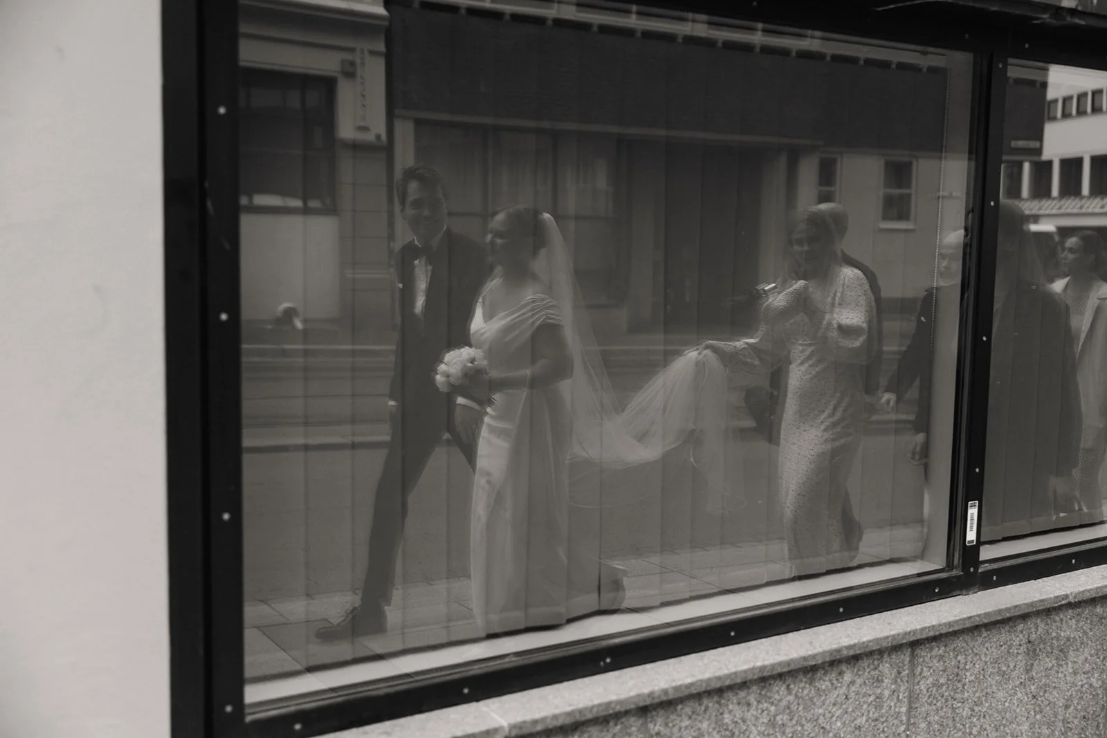 Refleksjon av brudeparet og gjester i et vindu