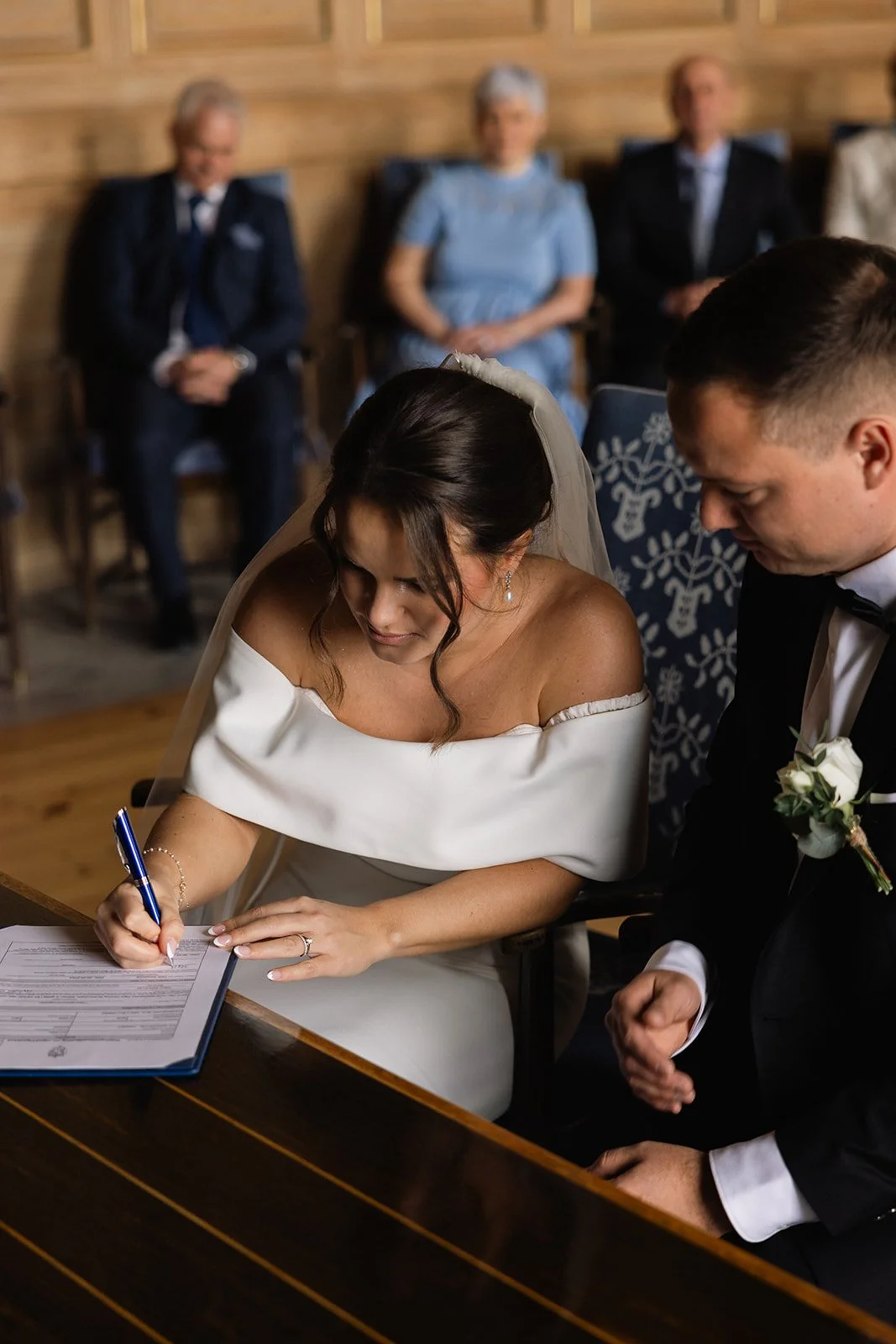 Brudeparet signerer et dokument under vielsen, mens utdelige gjester ser på.