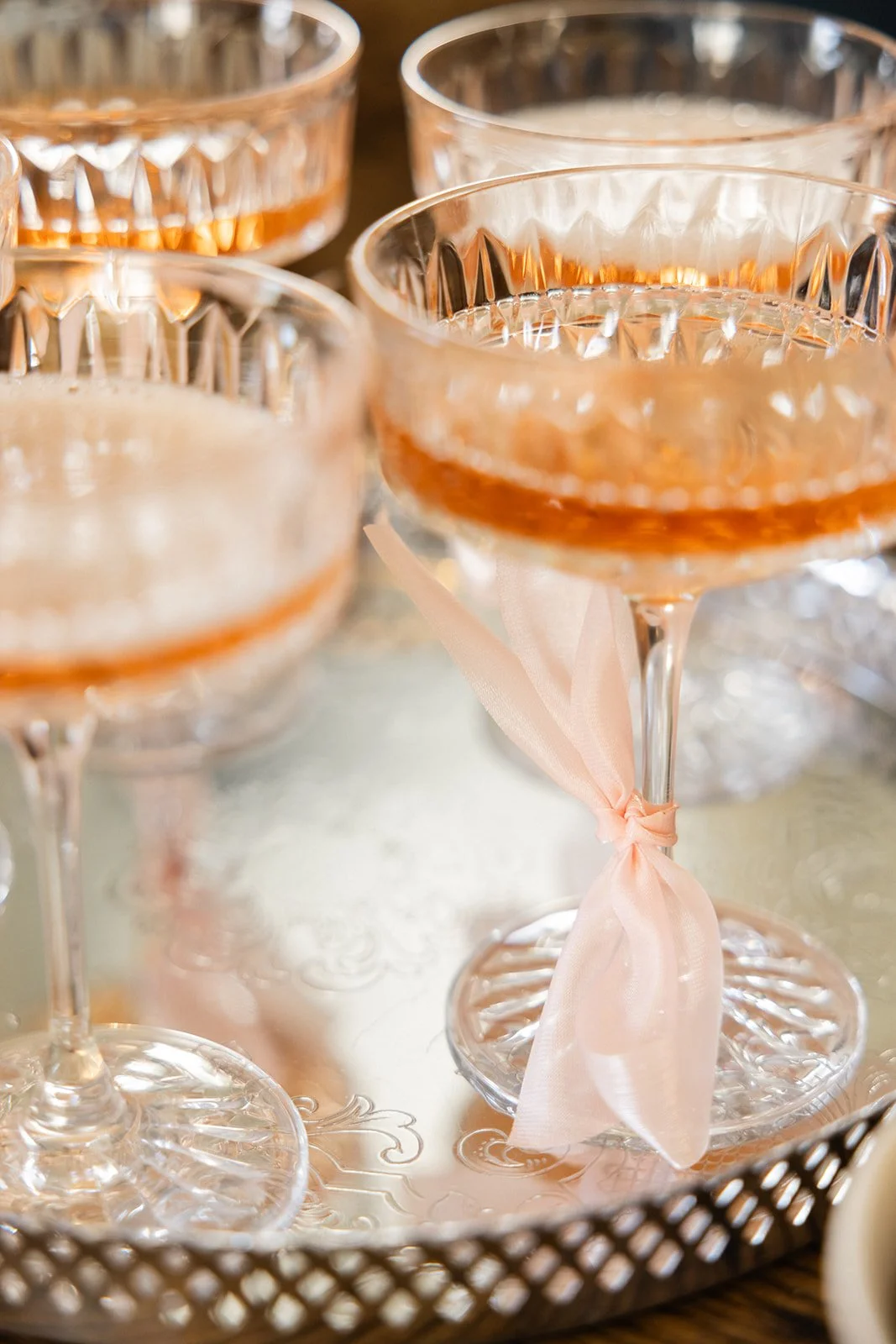 Fargede cocktailglass med rosa sløyfe, på en sølvfarget serveringsbrett.