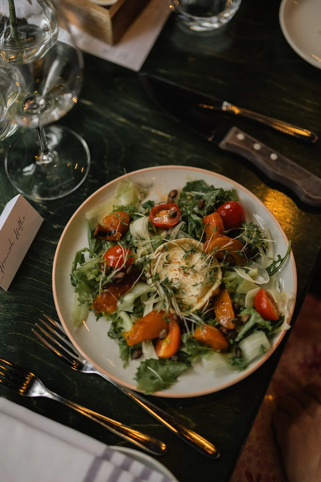 En tallerken med frisk salat med cherrytomater, salatblader, alfalfa, og en klatt med kremet urteost. Rester av glass og bestikk er rundt på bordet.