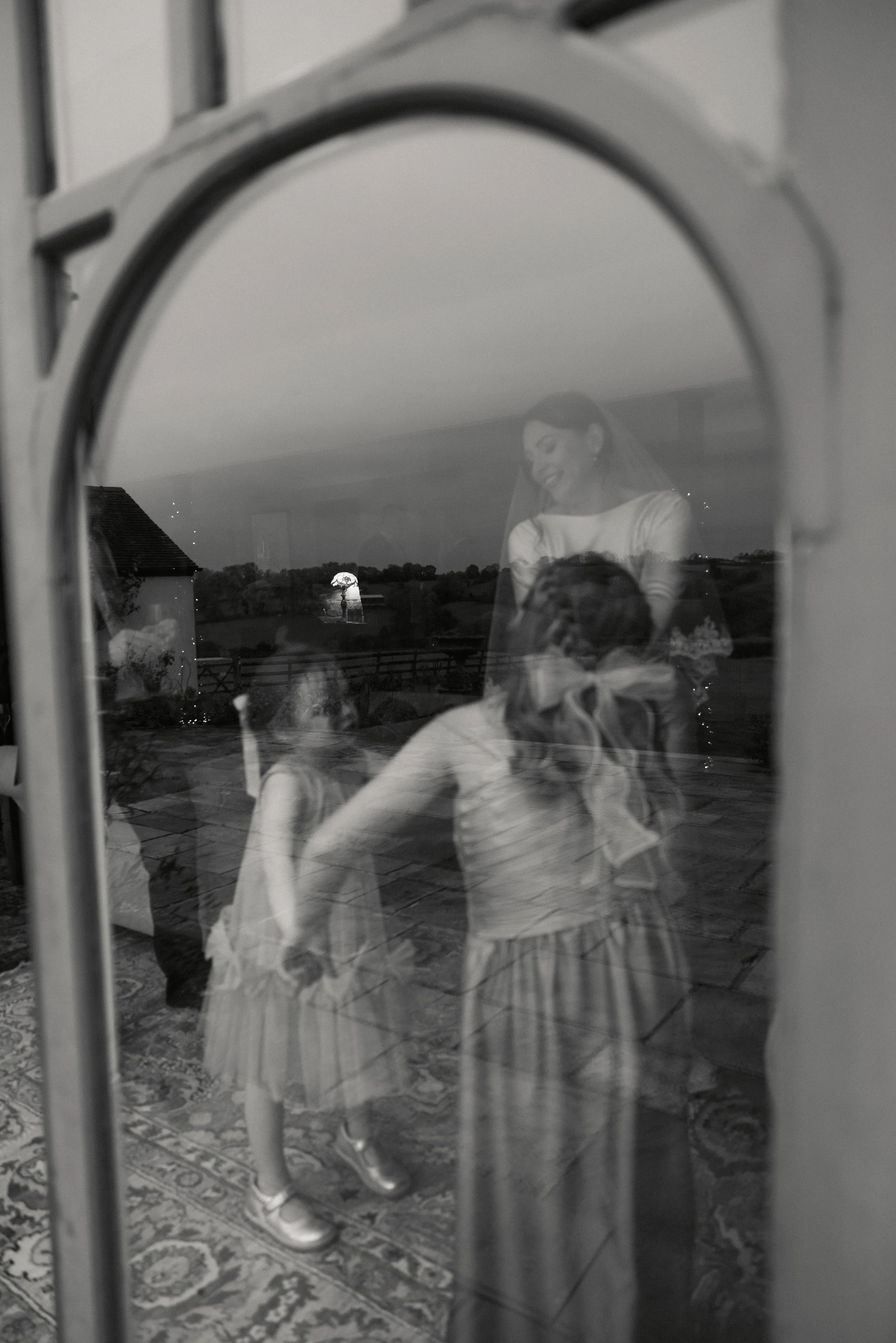 Refleksjon av kvinne og barn i vindu, med utsikt over landskap og solnedgang i bakgrunnen