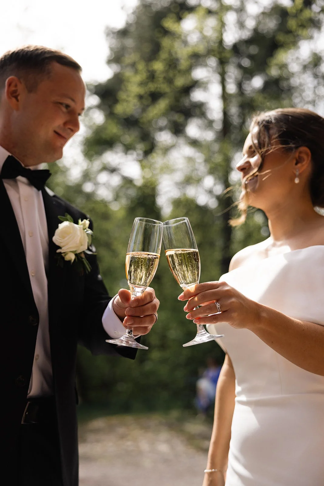 Et bryllupsscene med en brud og en brudgom som skåler med champagne utendørs.