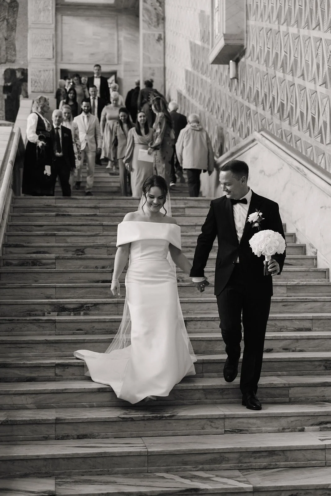 Et brudepar går nedover trappen under vielsen, omringet av familie og venner.