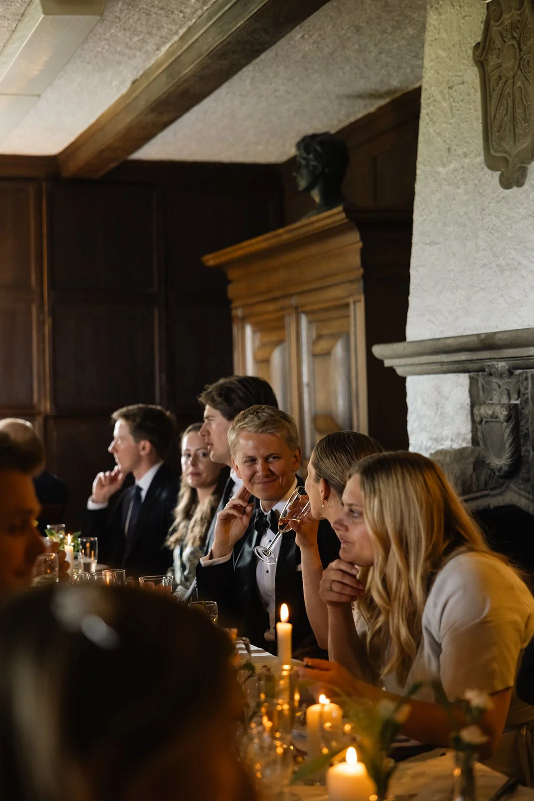 Gjestene sitter ved et langbord med stearinlys og deler en sosial stund.