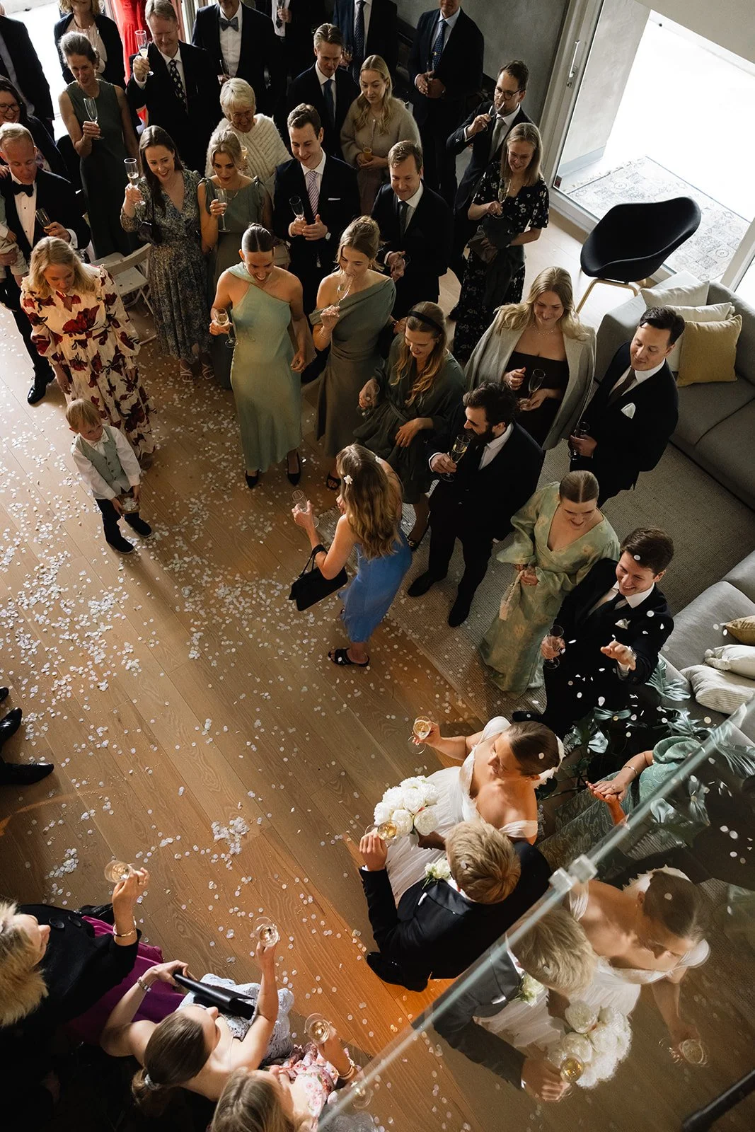 Brudeparet kysser under sin vielse i stuen, omgitt av familie og venner som feirer med champagne, alte på gulvet og konfetti.