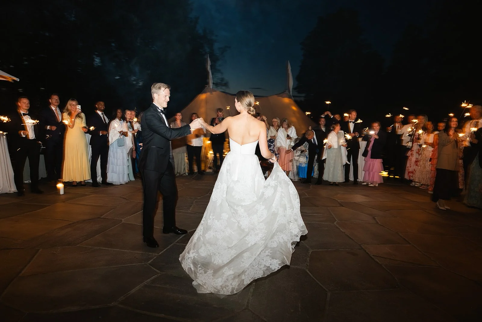 Bryllupspar danset i utendørs bryllupsmiljø om natten med gjester som holder lyslykter rundt dem.