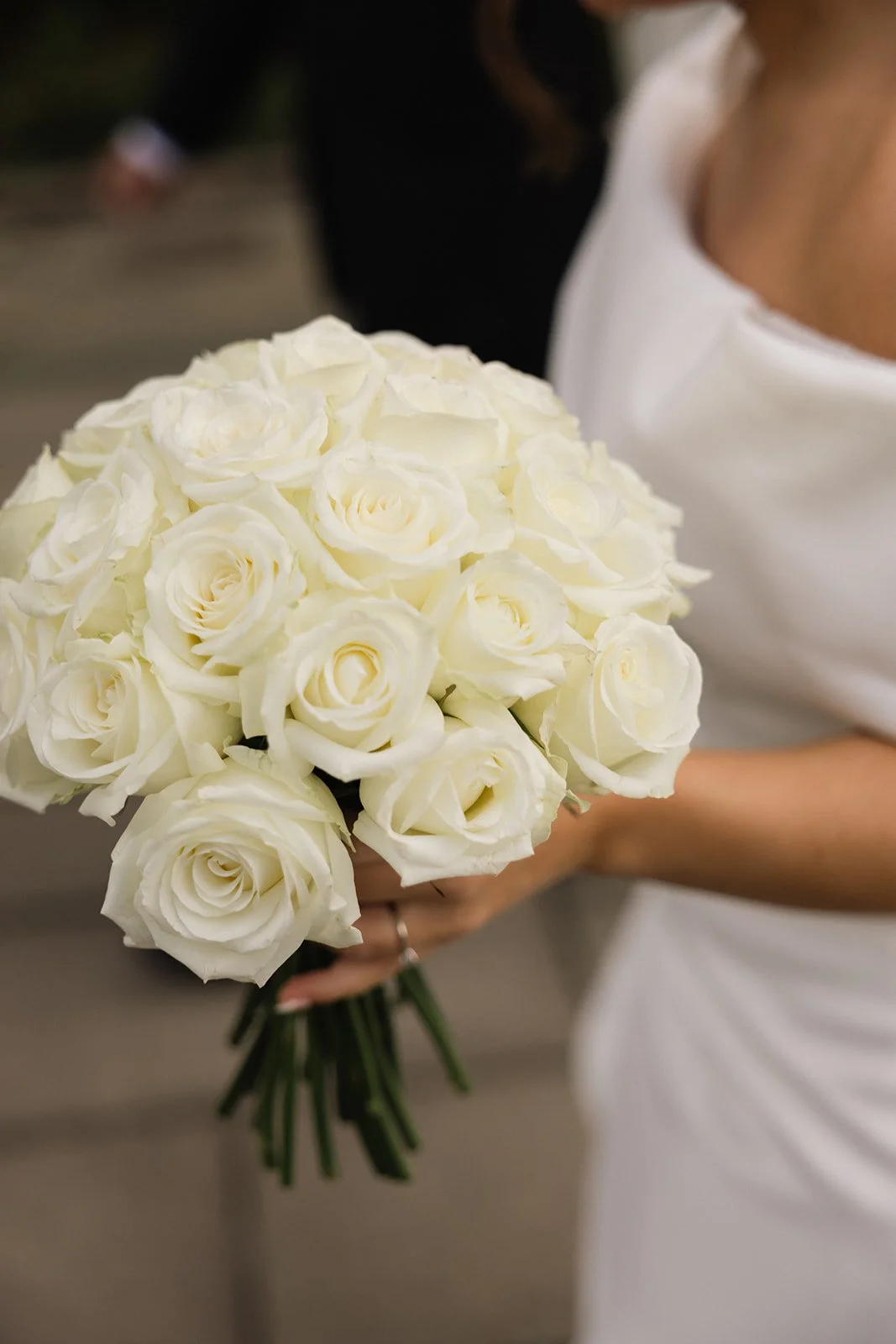 Nærbilde av en Person som holder en stor bukett hvite roser, delvis iført en hvit kjole.