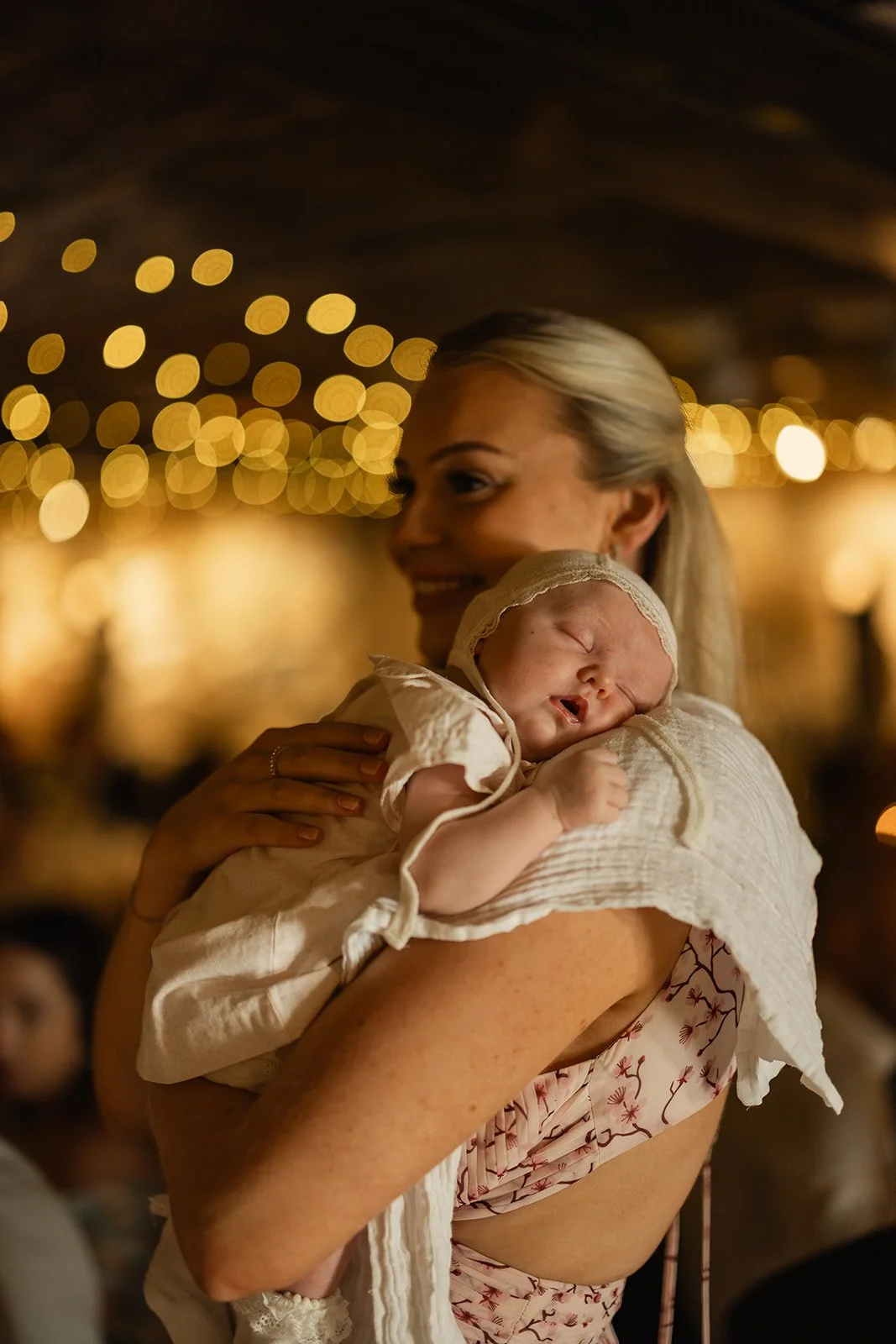 En kvinne holder en sovende baby i armene, omgitt av varme lys.