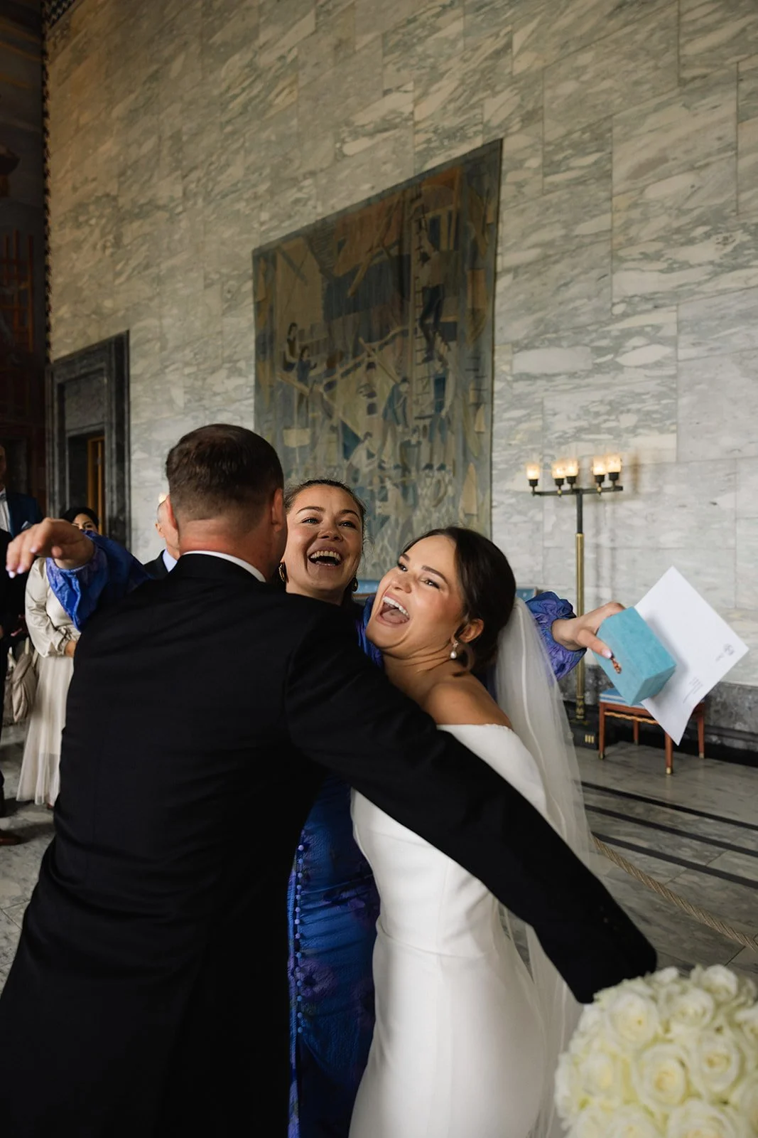 To personer i bryllupsklær som klemmer hverandre og ler i en stor, elegant hall