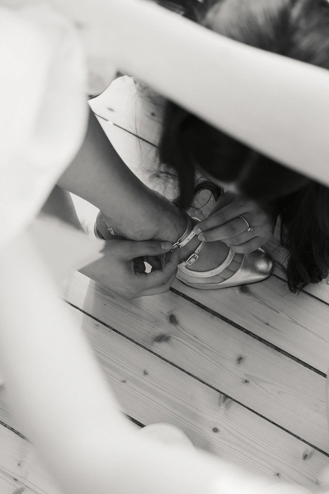 Person som blir hjulpet med å lukke en sko, tatt fra en vinkel ovenfra, i svart-hvitt.