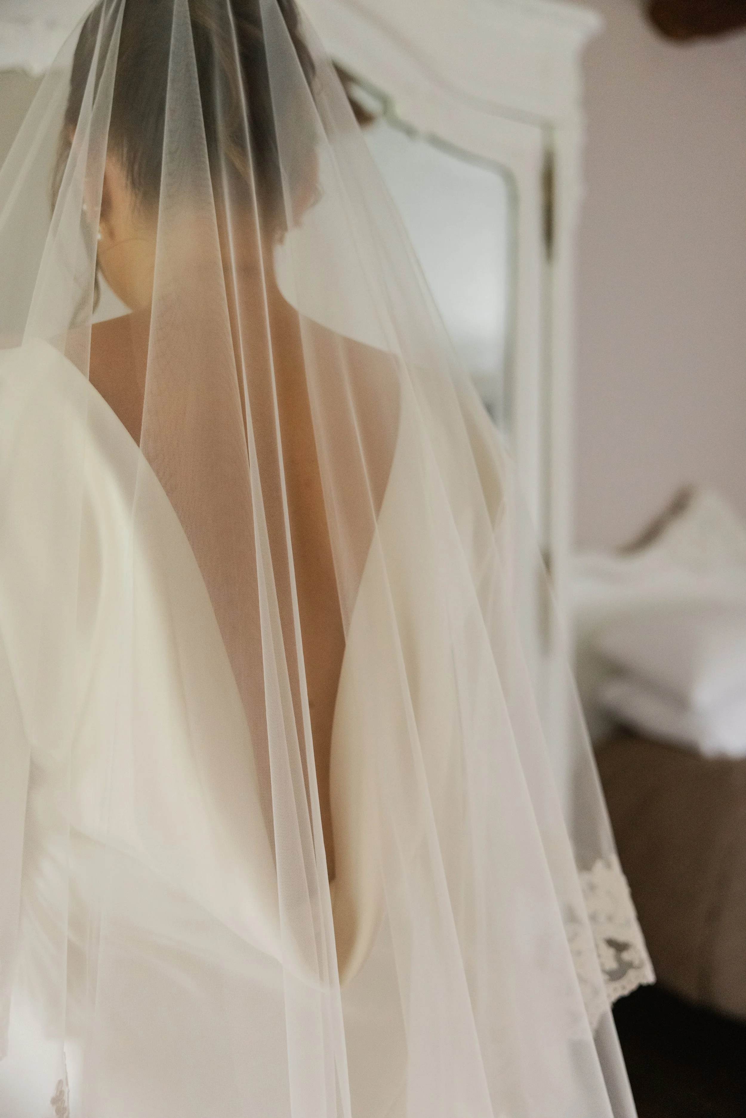 Kvinne i brudekjole med slør, sett fra siden i et rom med et speil i bakgrunnen.