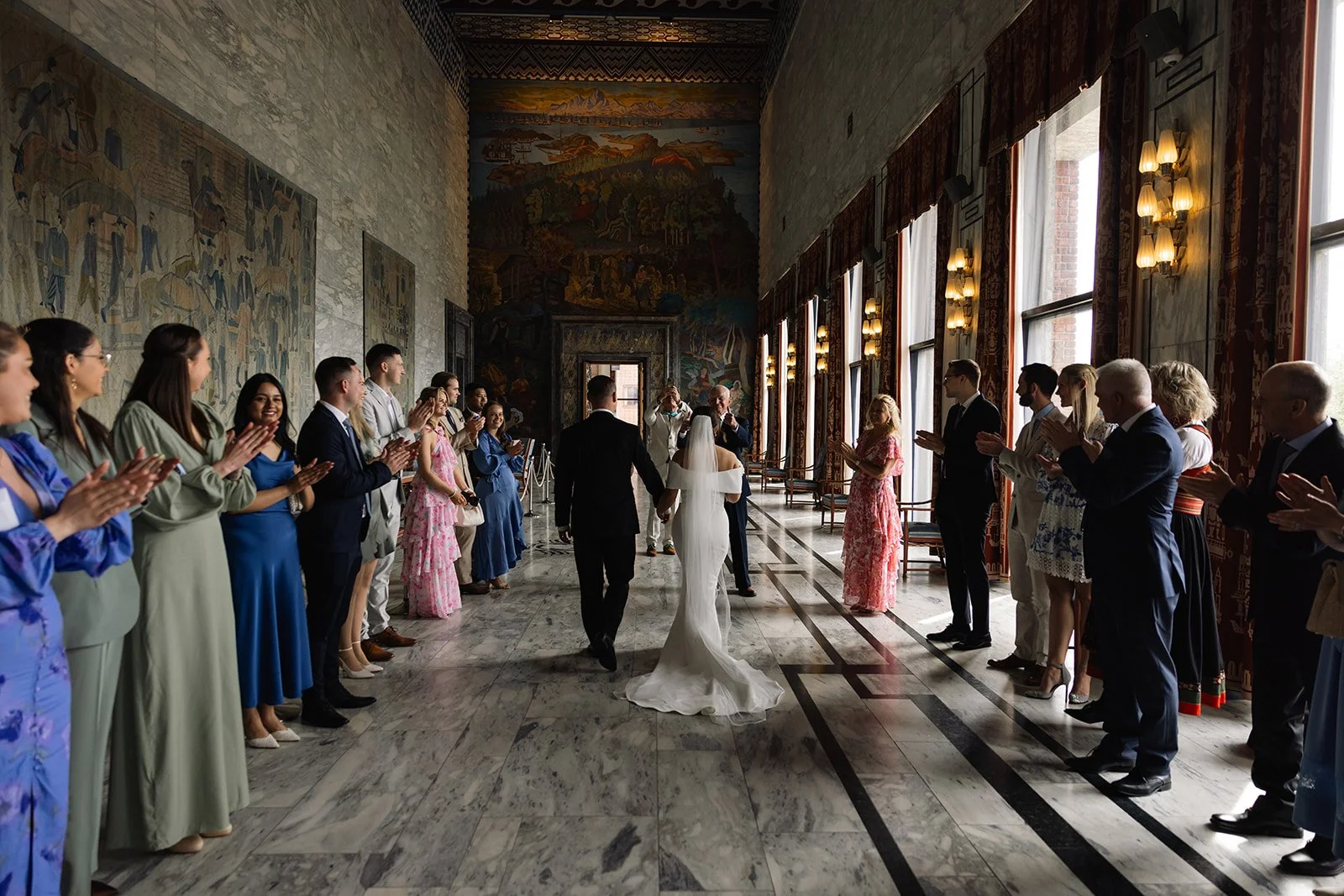 Et bryllup med bruden og brudgommen som går hånd i hånd inn i rommet, omgitt av venner og familie som applauderer.