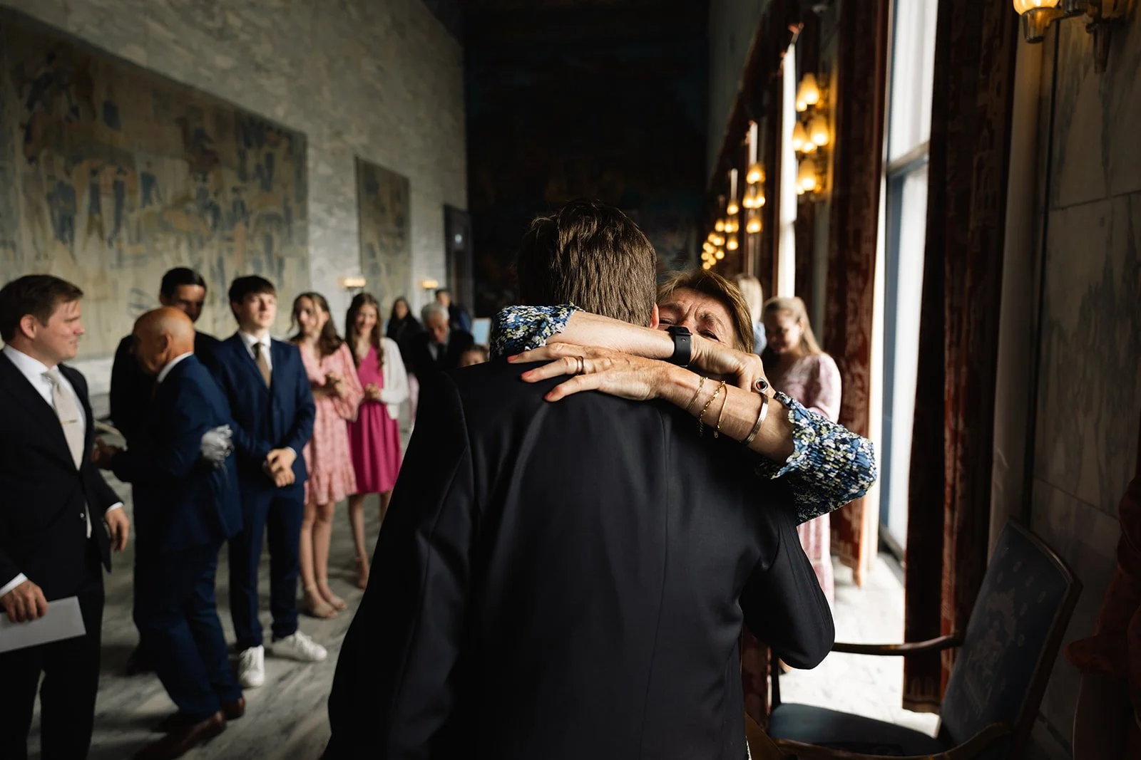 To personer omfavner hverandre i en offentlig setting, med flere mennesker i bakgrunnen.