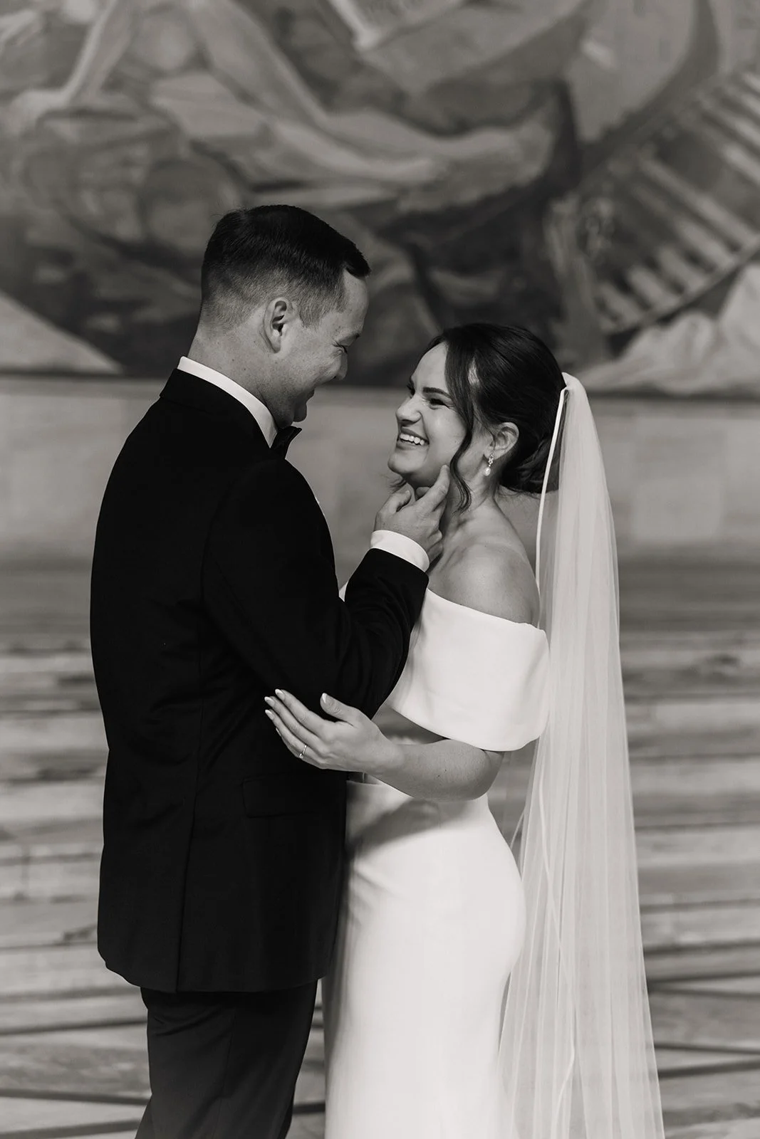 Et lykkelig brudepar i bryllup, hvor mannen ler og holder kvinnens hake mens hun smiler bredt.