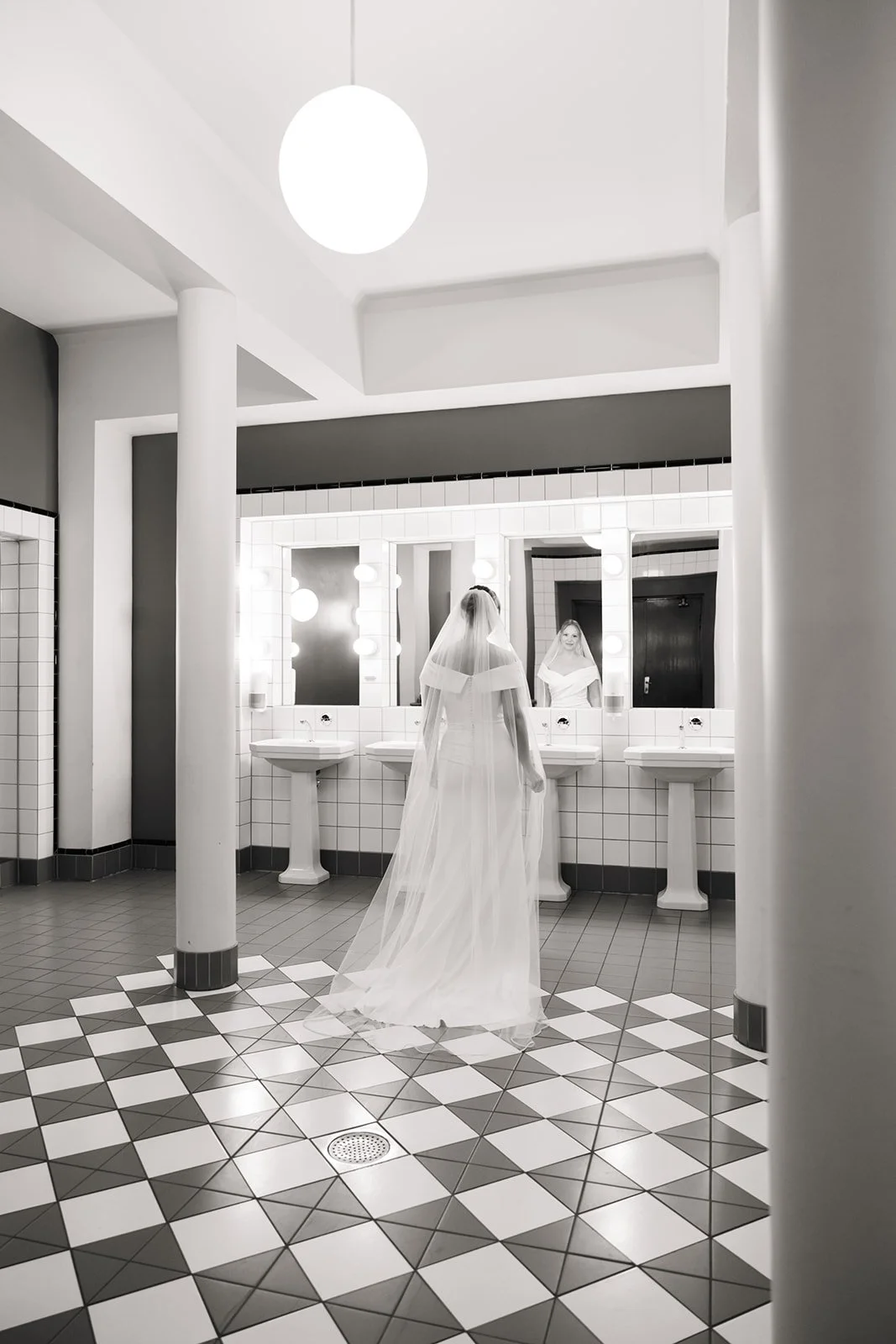 En kvinne i brudekjole ser på seg selv i et stort speil på toalettet.