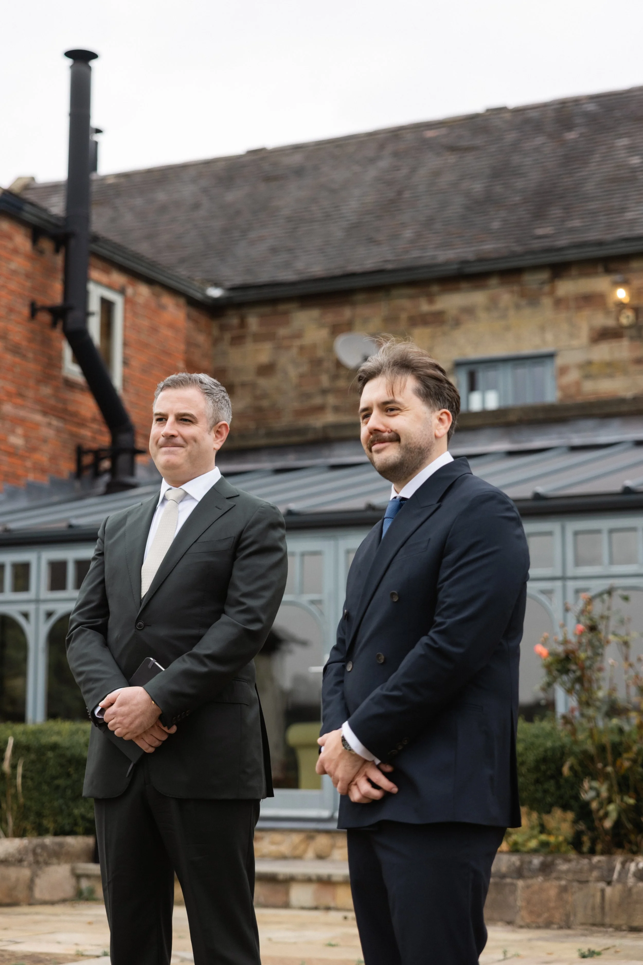 To menn i formelle dresser står utendørs, med en bygning i bakgrunnen.