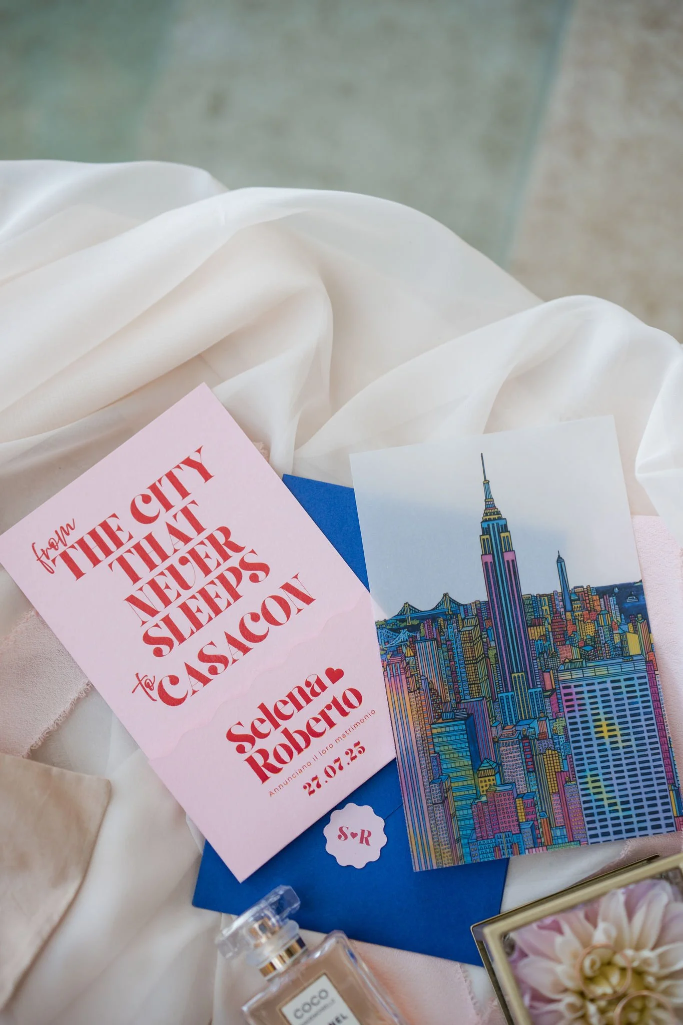 Colorful illustrated New York City skyline with the Empire State Building, pink and blue tones, on a wedding invitation card.