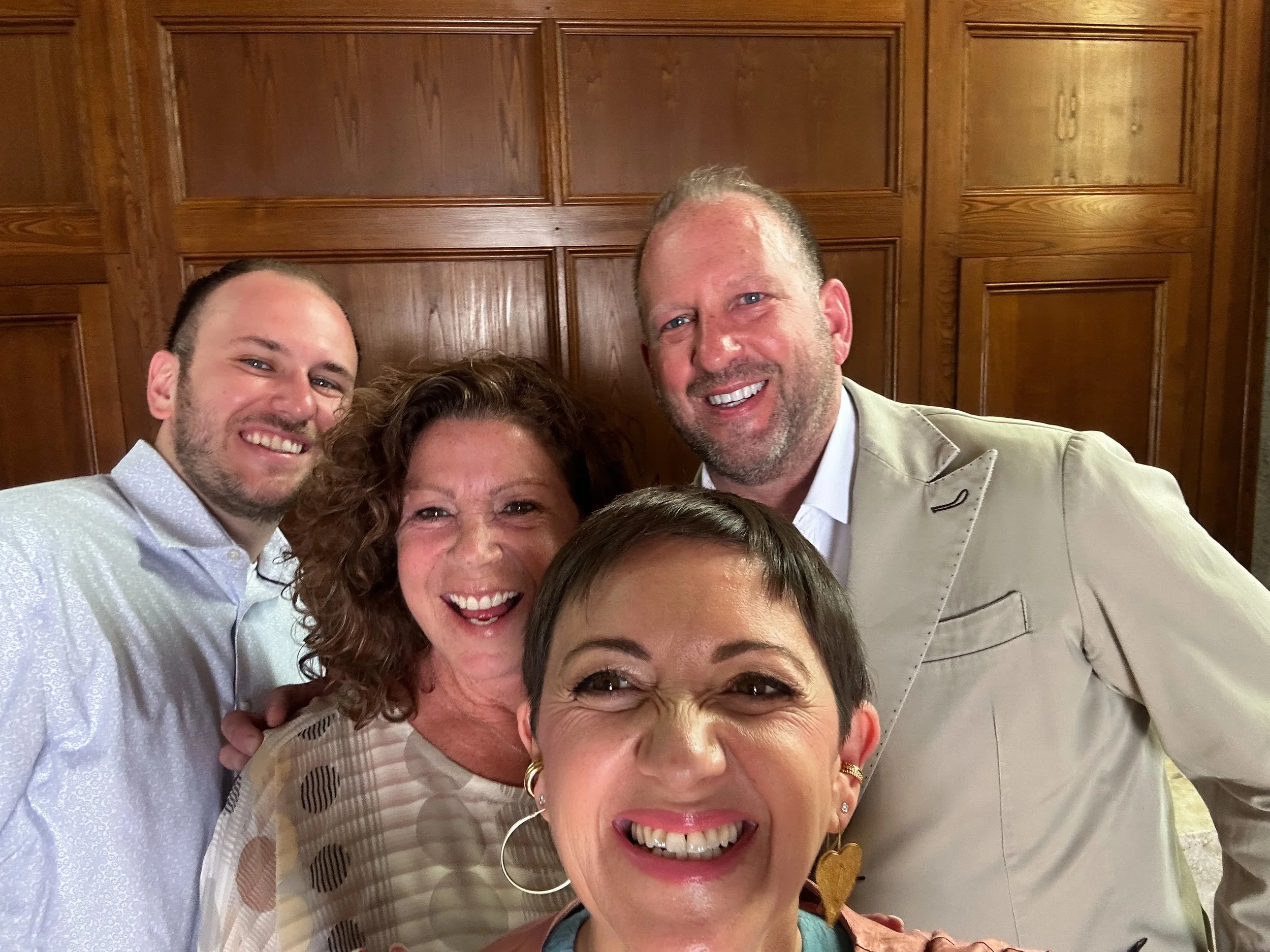 Group of five smiling people taking a selfie in front of a wood-paneled wall.