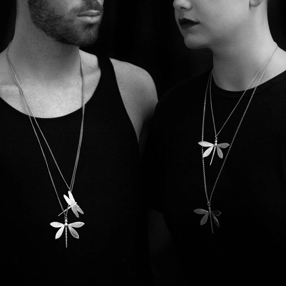 Close-up of two people wearing black tops and dragonfly necklaces in a black-and-white photograph.