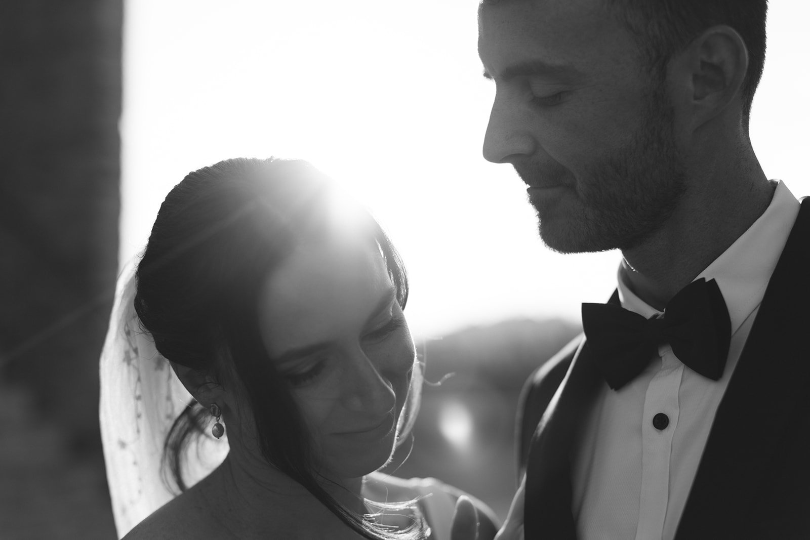 A black and white photo of a bride and groom on their wedding day, with the sun setting in the background, creating a romantic silhouette scene.