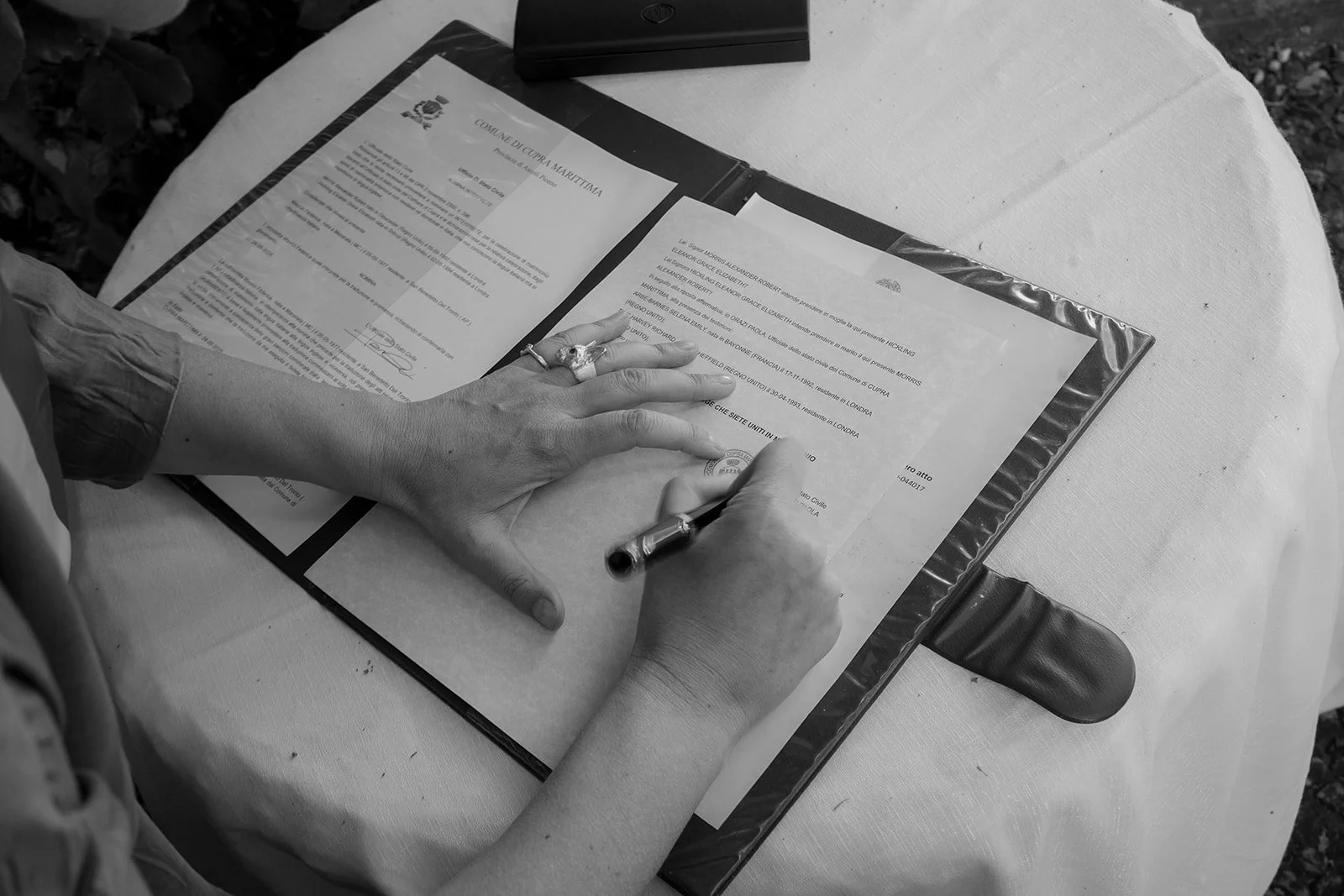 Person signing a document on a table outdoors filled with papers and a pen.