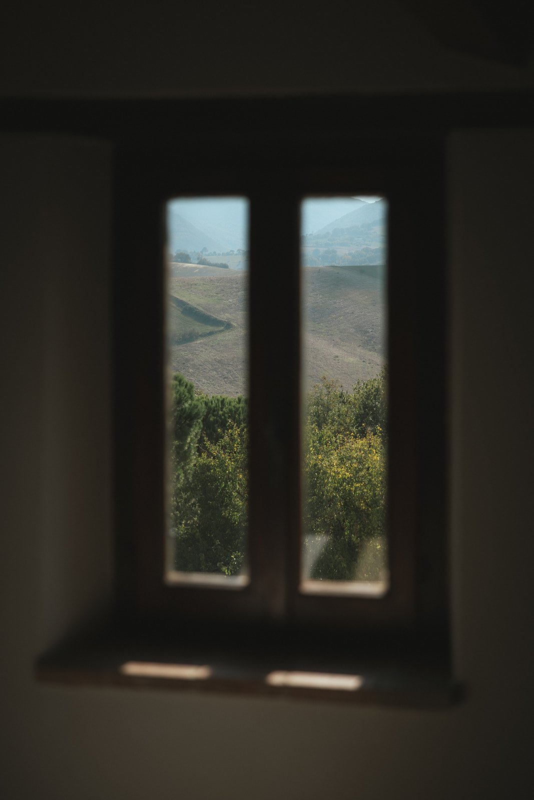 View through a small window showing a landscape of rolling hills, green trees, and a distant mountains.