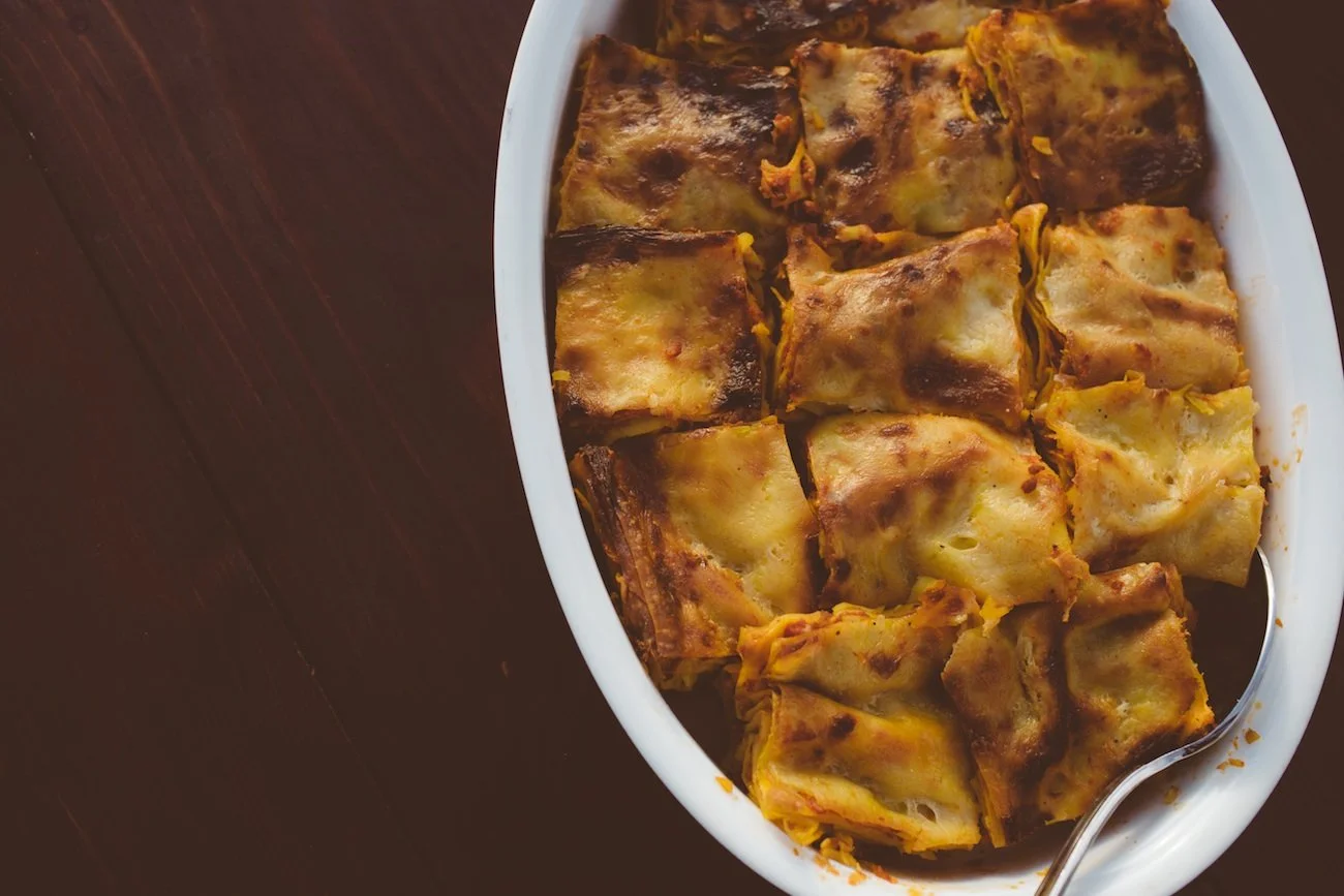 Baked ziti with melted cheese in a white oval dish on a dark wooden surface.