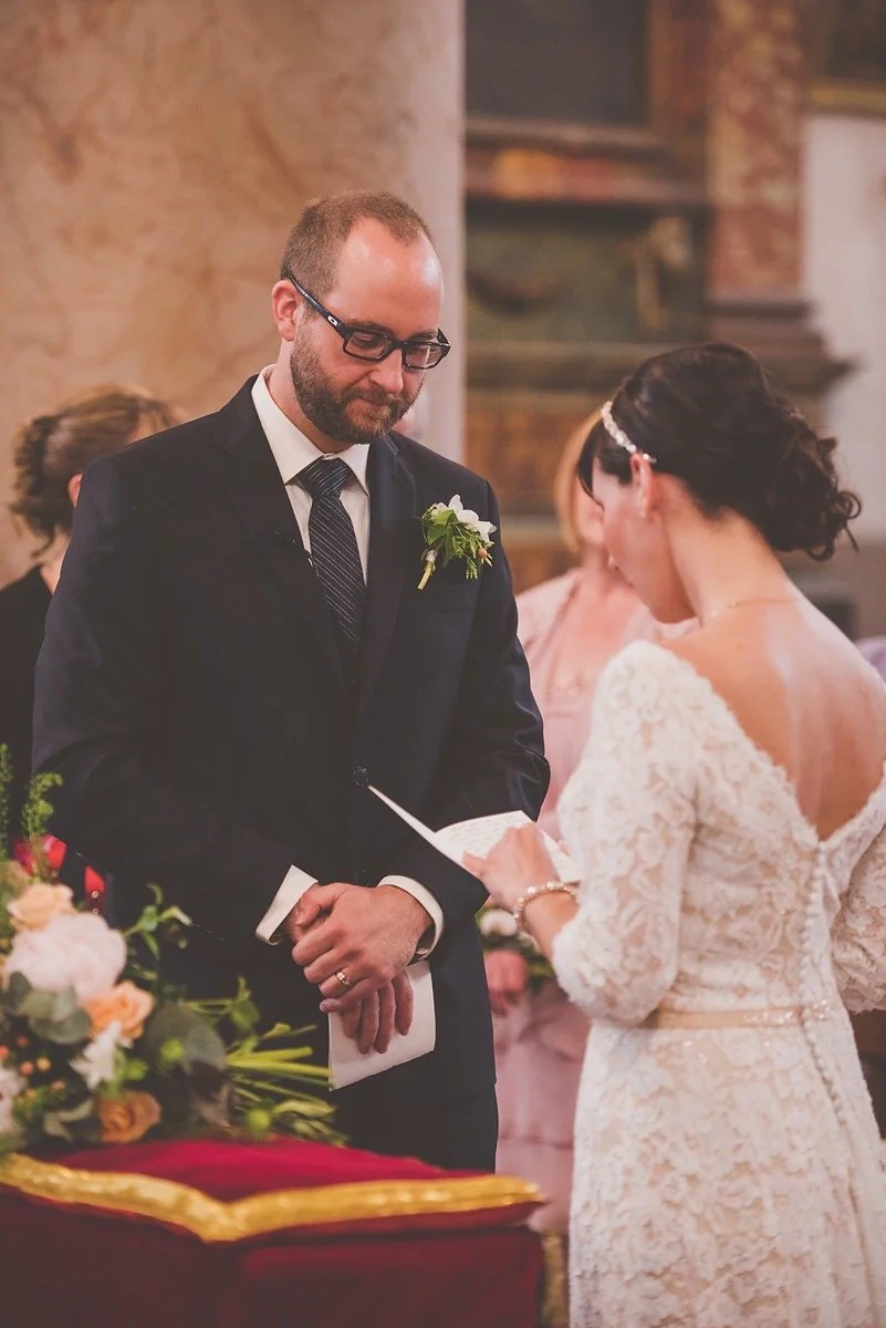 A man and woman exchanging wedding vows during a ceremony inside a church or chapel, with flowers and decorations in the foreground.