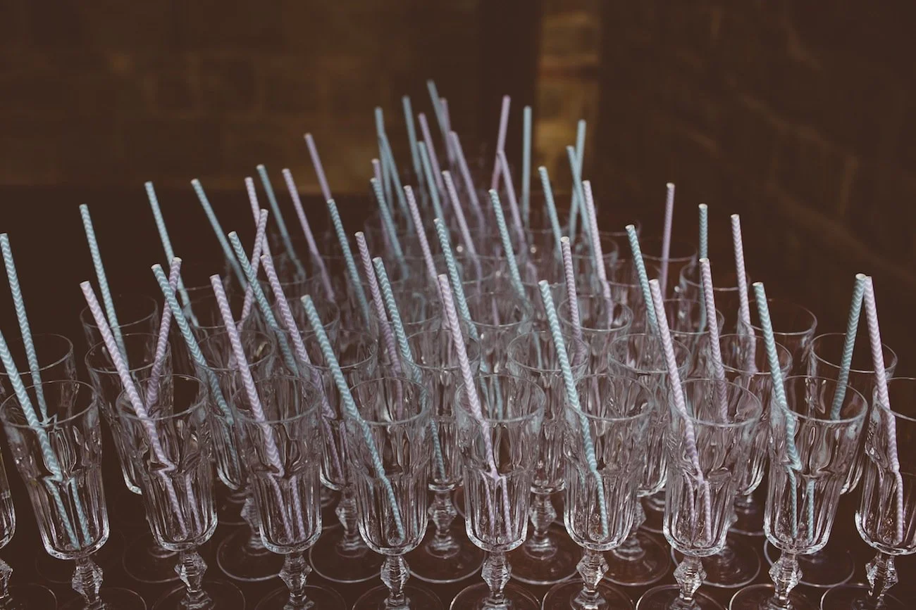 A collection of empty crystal shot glasses with pink and blue striped cocktail straws inside each glass.