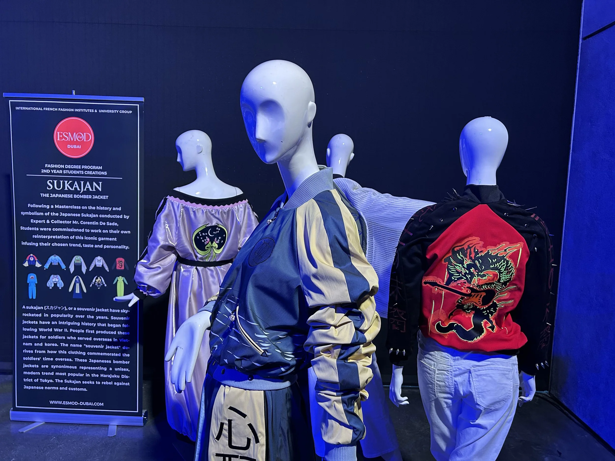 Three mannequins dressed in Japanese bomber jackets with unique designs, displayed in an exhibition with a informational sign about Sukajan jackets and their history.