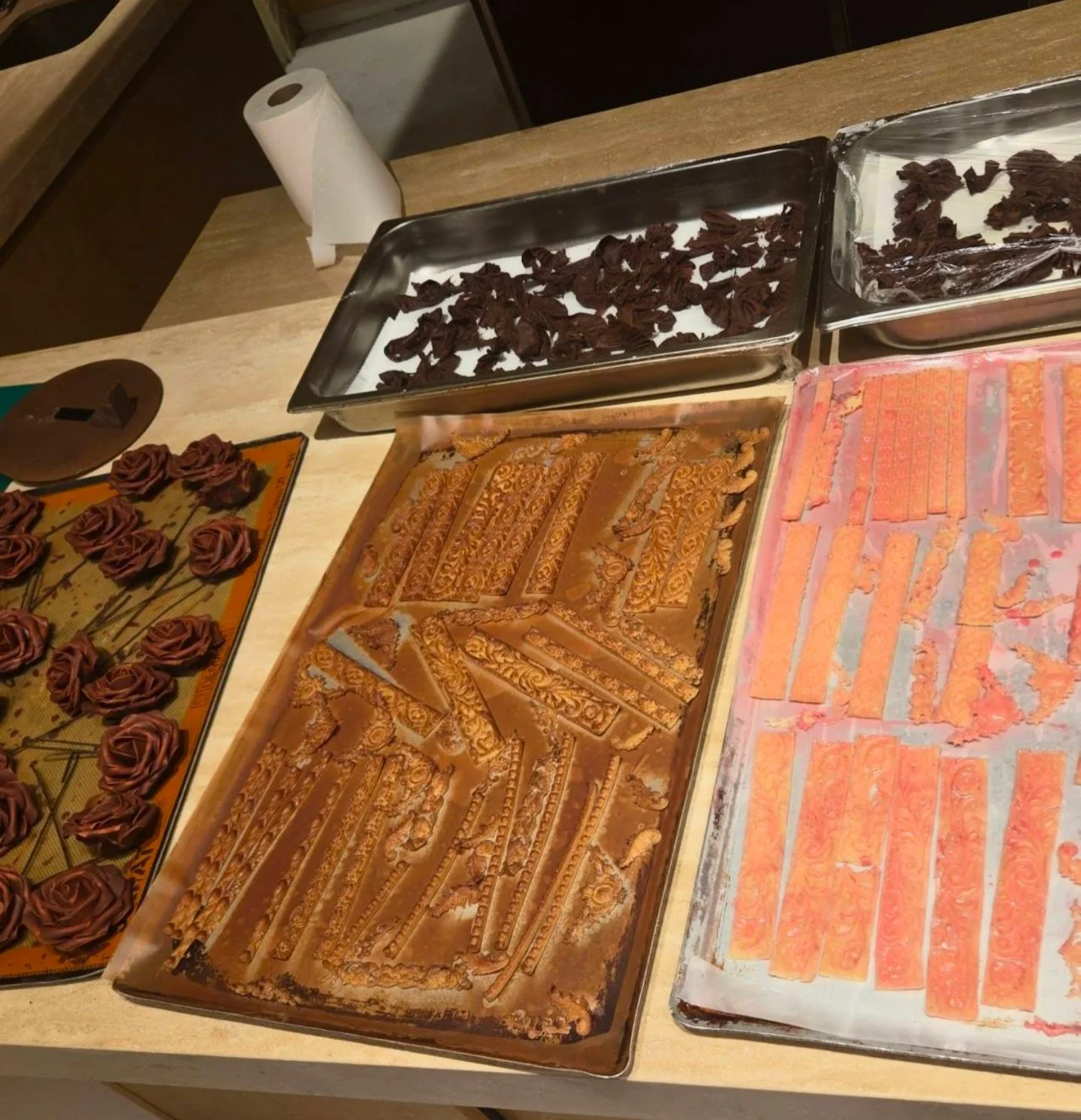 Baking sheets with decorated cookies, some in the shape of roses, and painted cookies with orange and pink icing, on a wooden table.