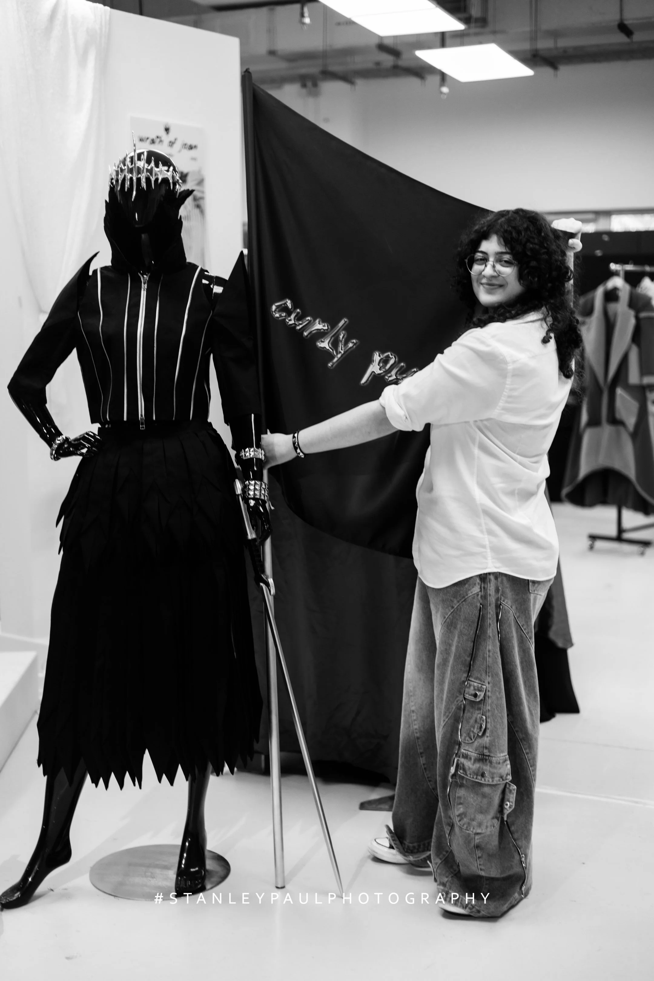Tugali Jarrouj, founder and creative director of Curly Punk, photographed holding the brand’s flag alongside a mannequin, reflecting the label’s identity, authorship, and design direction.