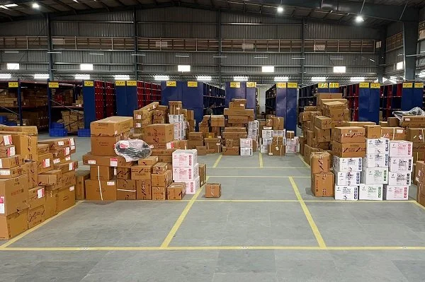 A warehouse with shelves filled with boxes and cartons, and many boxes stacked on the floor.